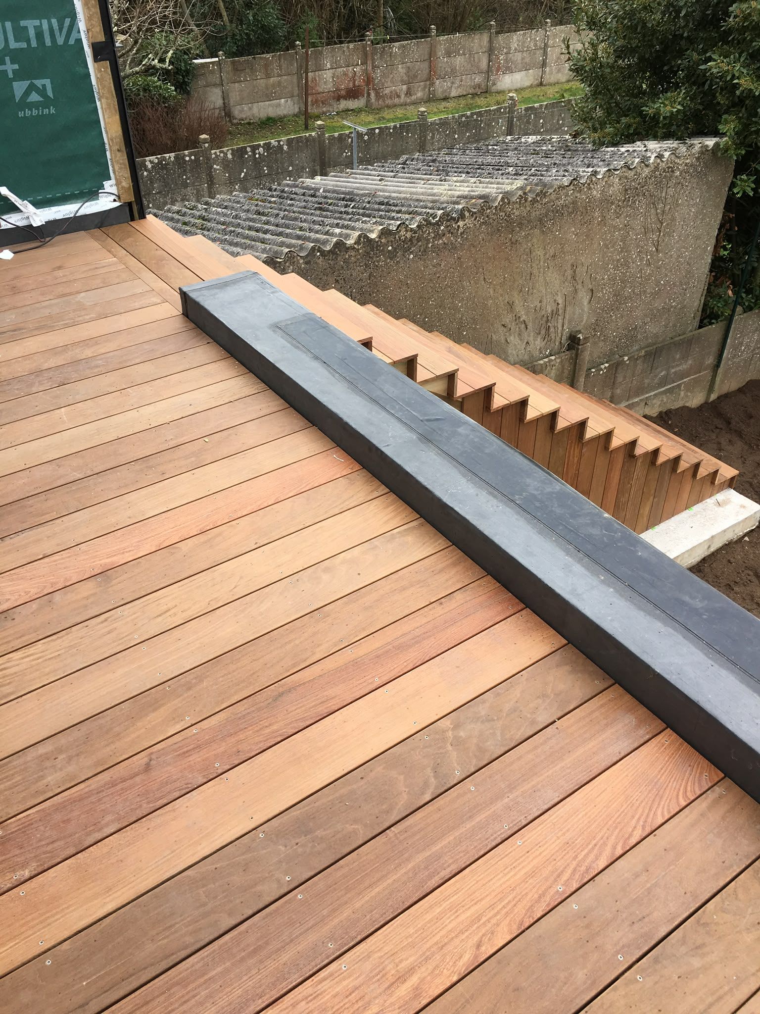 Terrasse en bois avec une longue poutre sombre et un escalier en béton longeant un canal d’eau