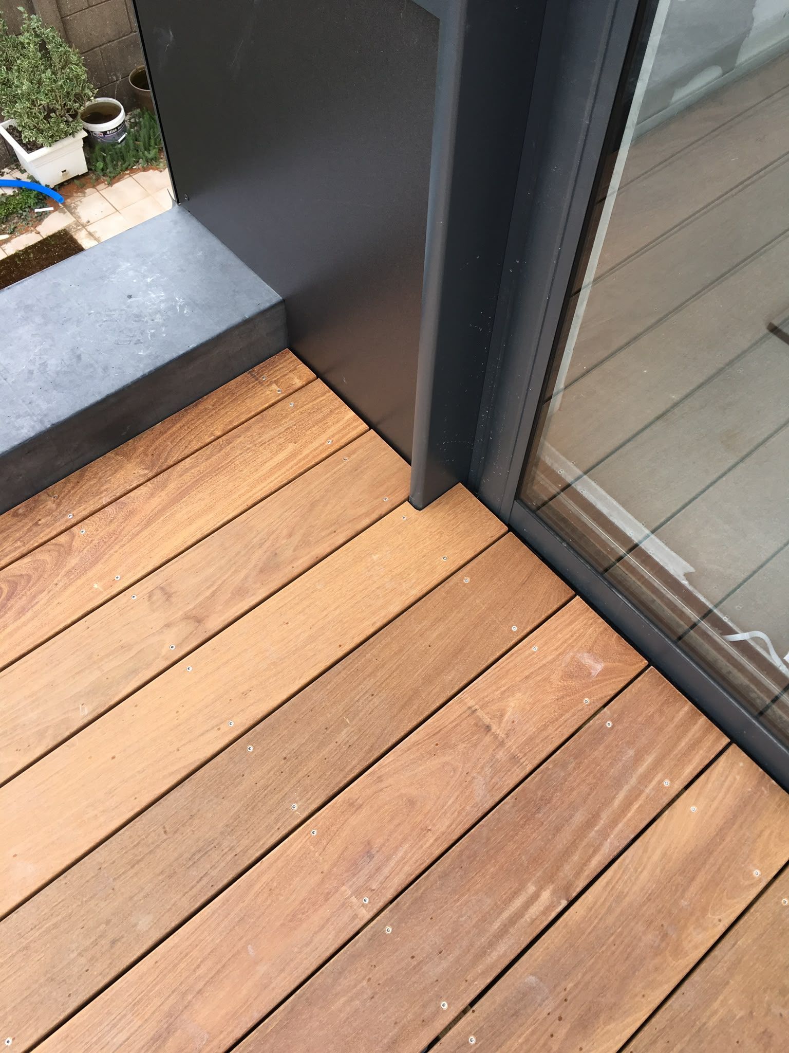 Terrasse en bois à côté d’une porte coulissante vitrée et d’un pilier extérieur sombre