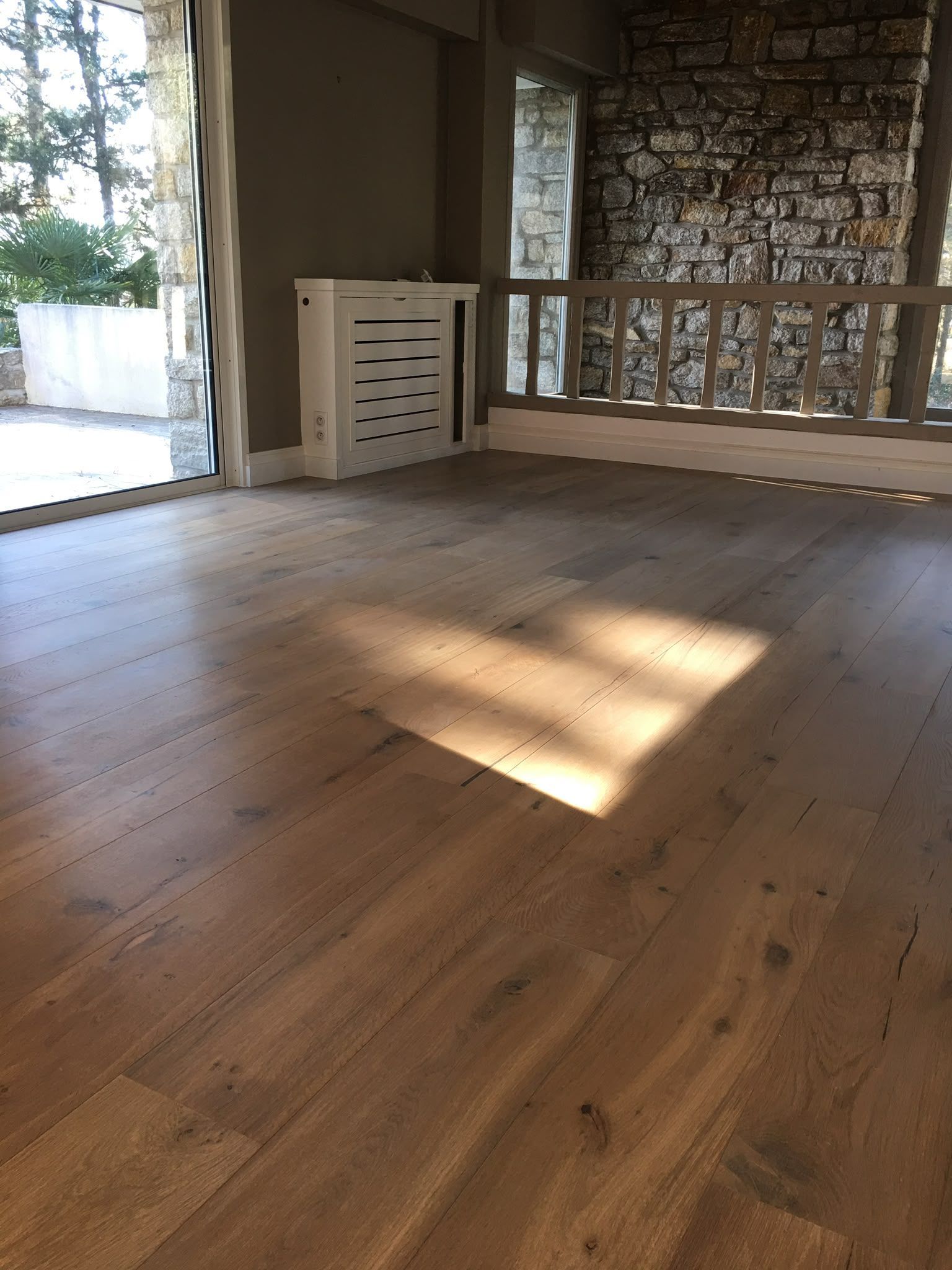 Pièce en bois vide baignée de soleil, avec un mur de pierre, une rambarde et une porte ouverte sur l’extérieur