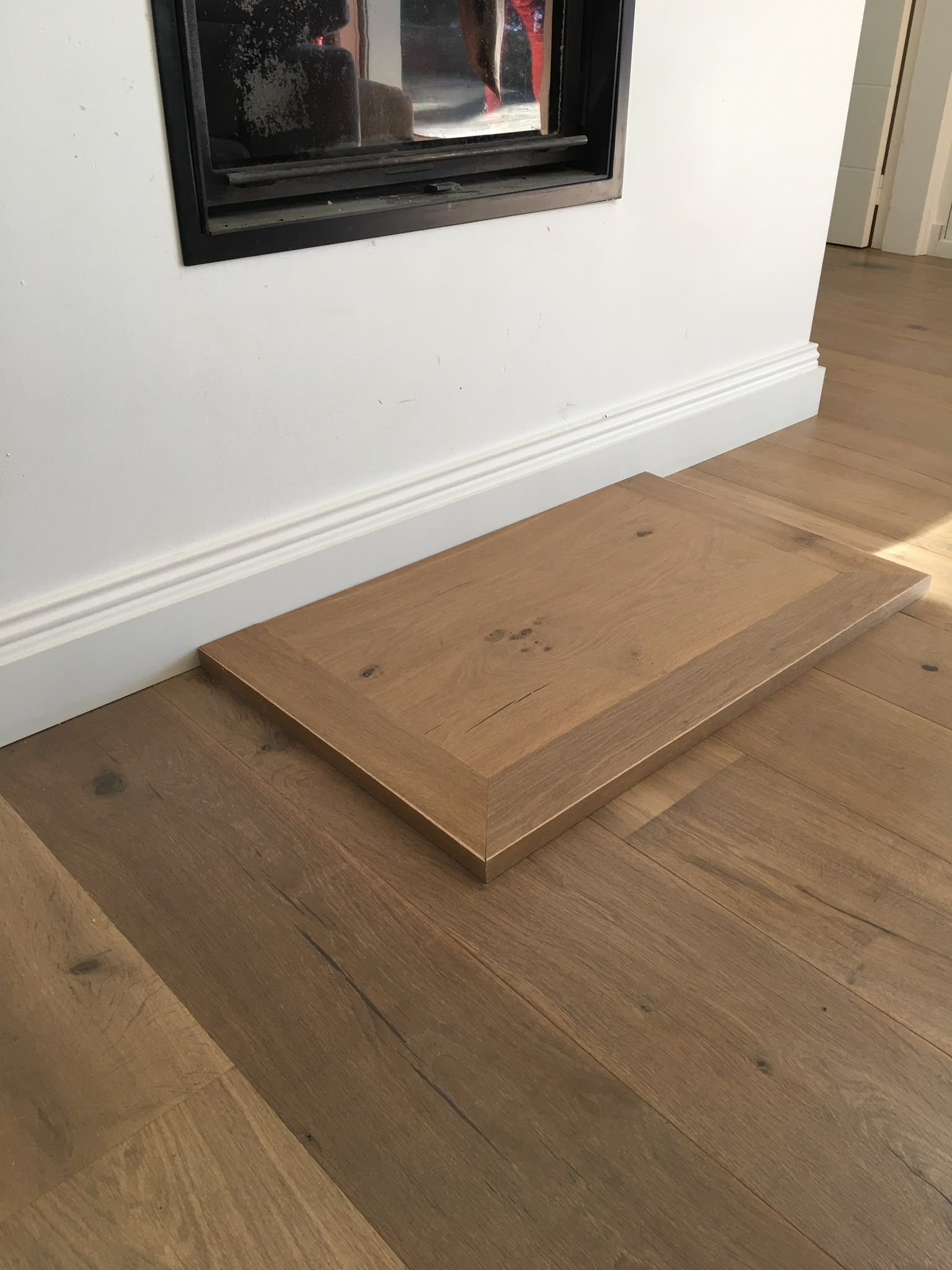 Une rampe en bois menant à une cheminée, à côté d’une plinthe blanche, sur un parquet en bois dur.