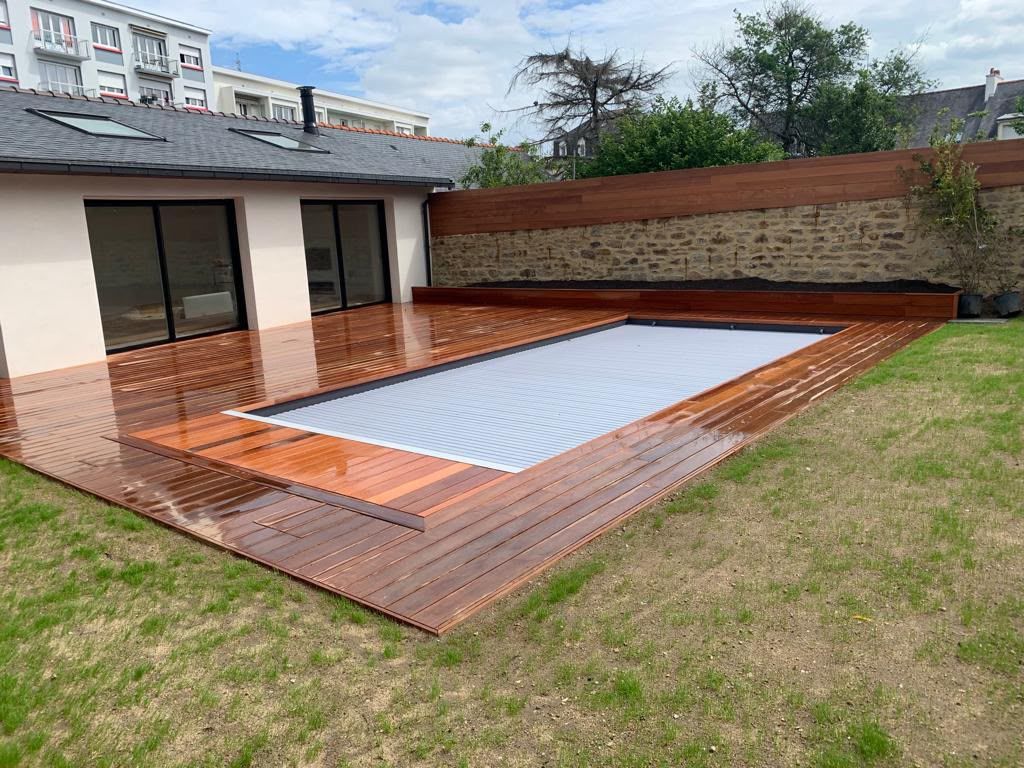 Piscine dans le jardin recouverte d’une bâche blanche, près d’une terrasse en briques et d’une pelouse