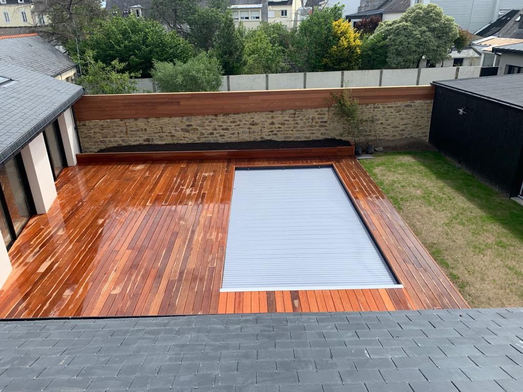 Terrasse en bois dans un jardin, avec une piscine ou un jacuzzi couvert, entouré d’une pelouse et d’une clôture