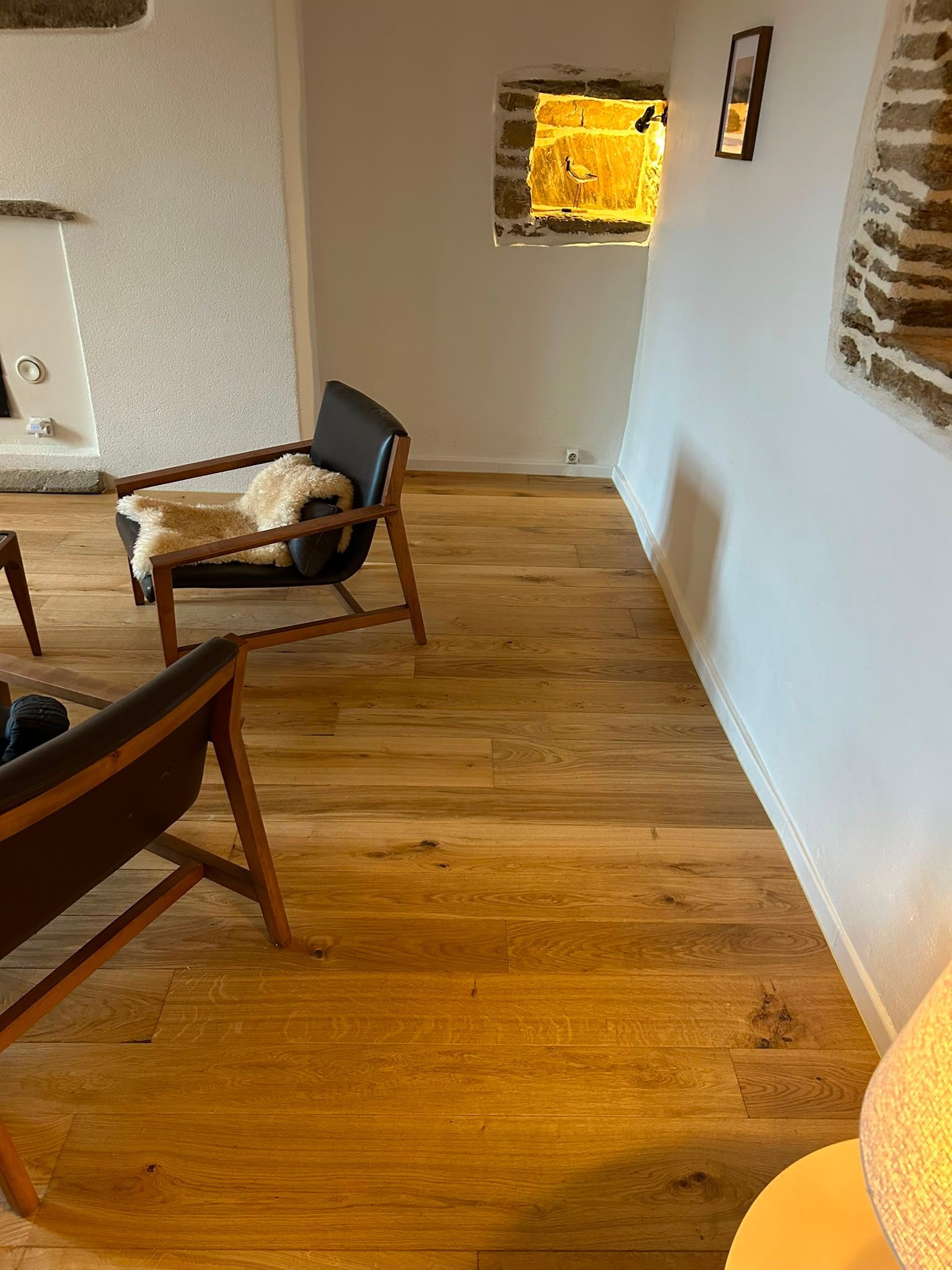 Salon au parquet avec des fauteuils modernes et une fenêtre lumineuse, vu depuis un couloir