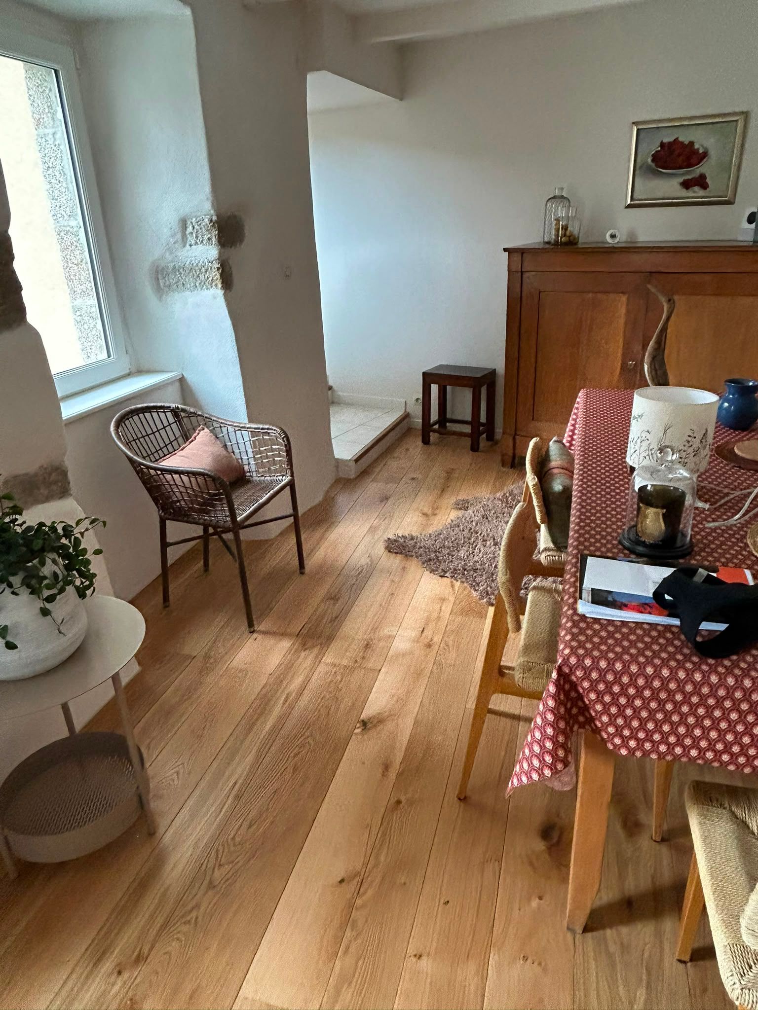 Salle à manger chaleureuse avec un parquet, une nappe à carreaux, des chaises et un petit buffet près d’une fenêtre.