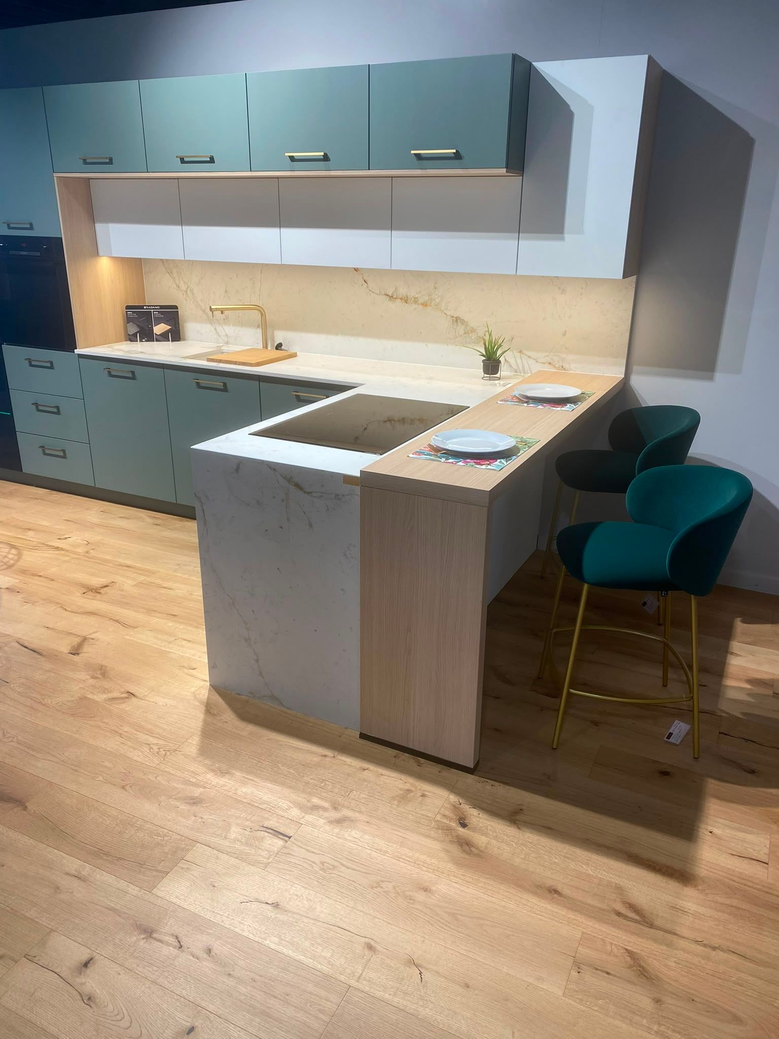 Cuisine moderne avec des placards gris, un îlot blanc, un parquet en bois et deux tabourets de bar bleu sarcelle