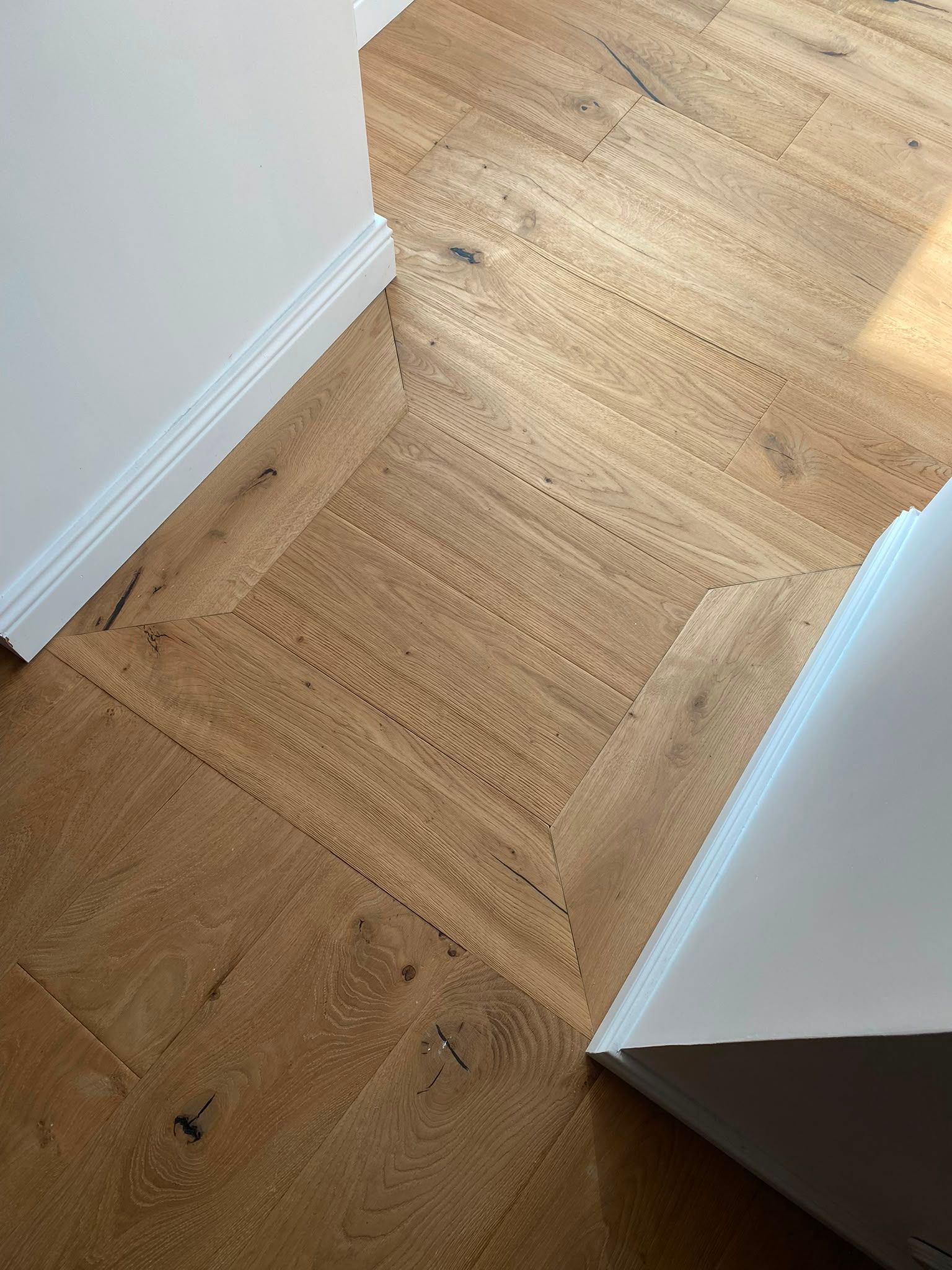 Couloir avec un parquet en bois, des murs blancs et une porte à droite