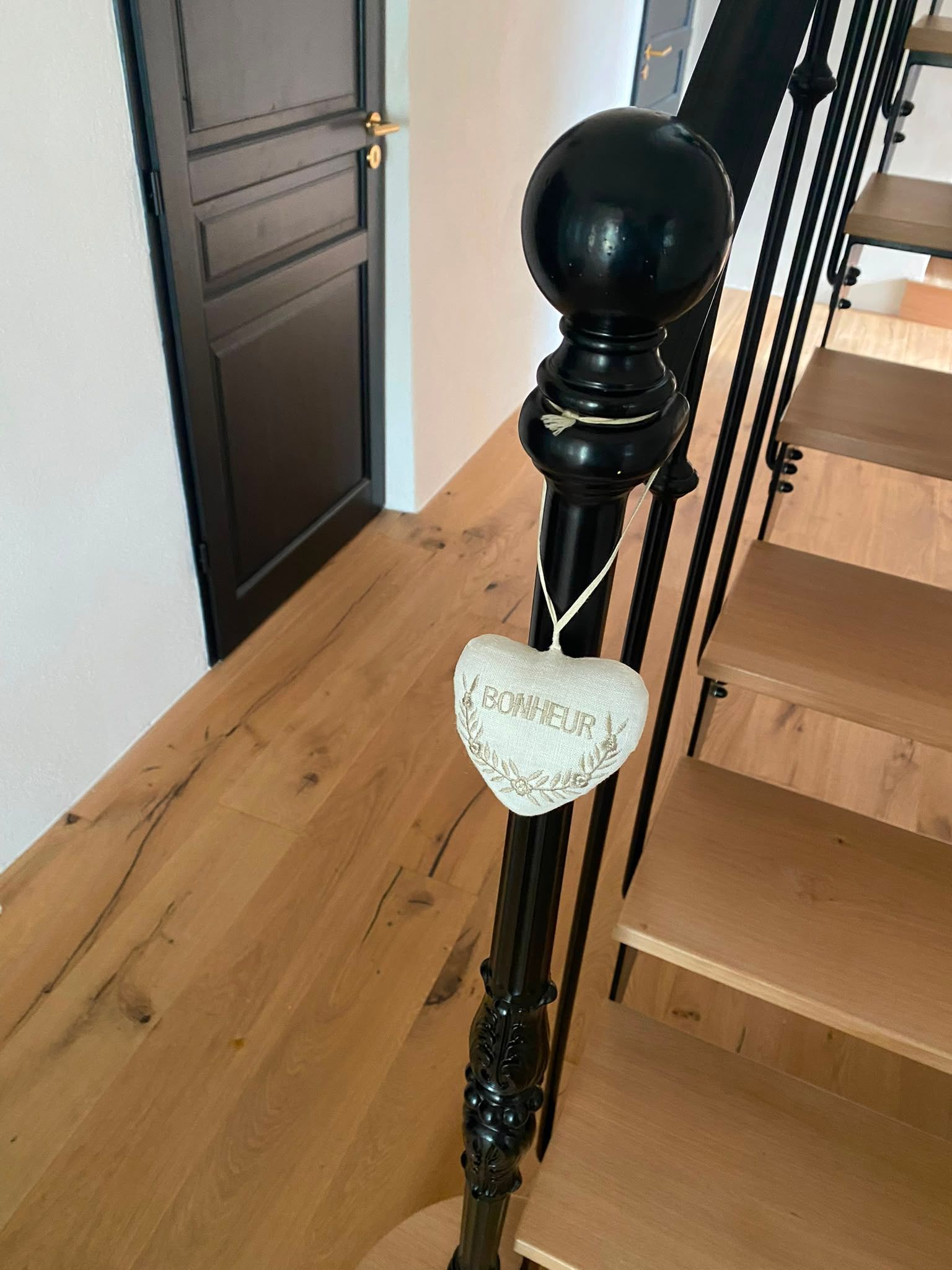 Rampe d’escalier noire avec une pancarte en forme de cœur suspendue à côté d’un escalier en bois, dans un couloir.