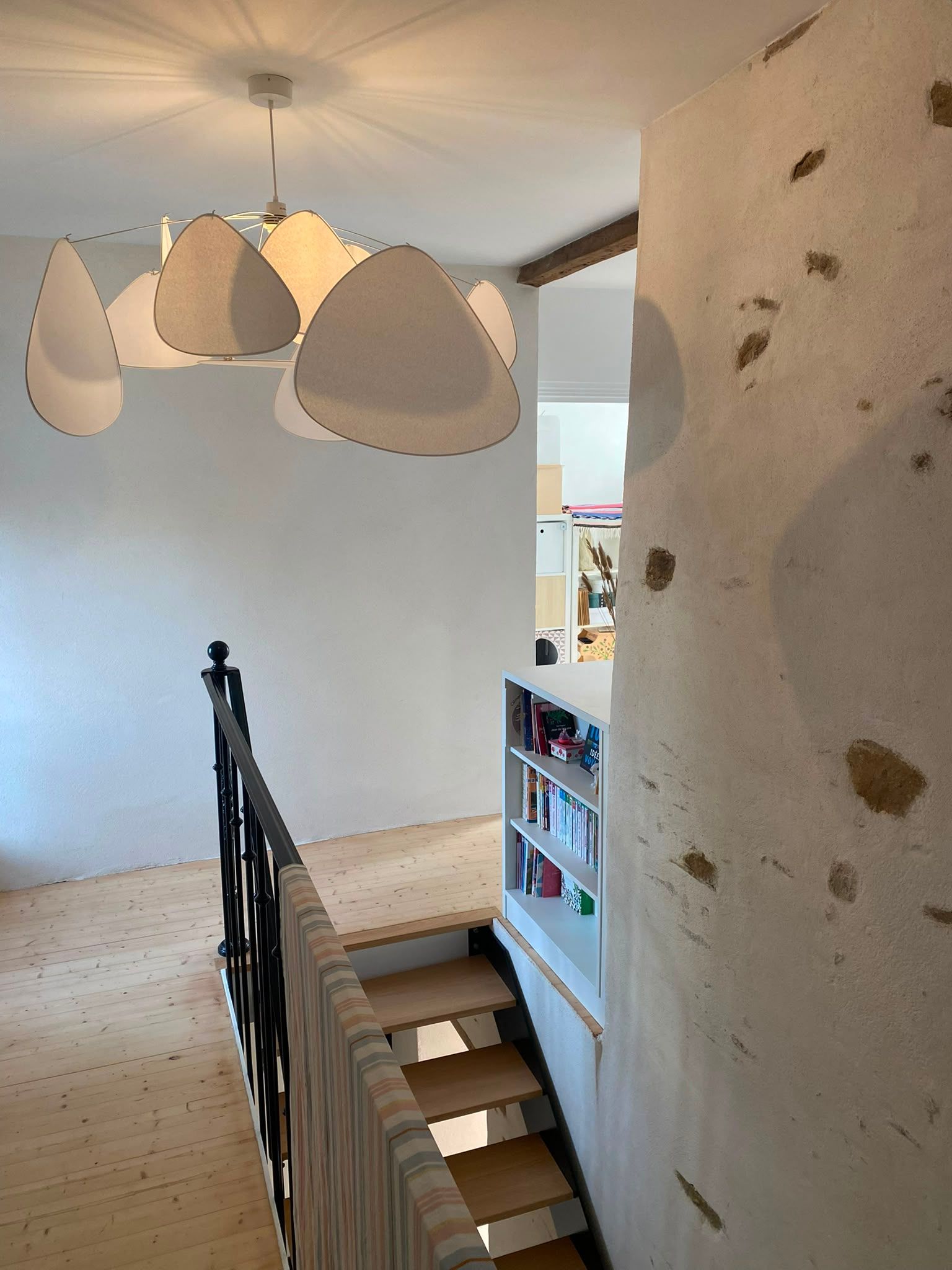 Cage d’escalier aux murs blancs, éclairée par des suspensions, avec une vue sur une pièce dotée de bibliothèques.