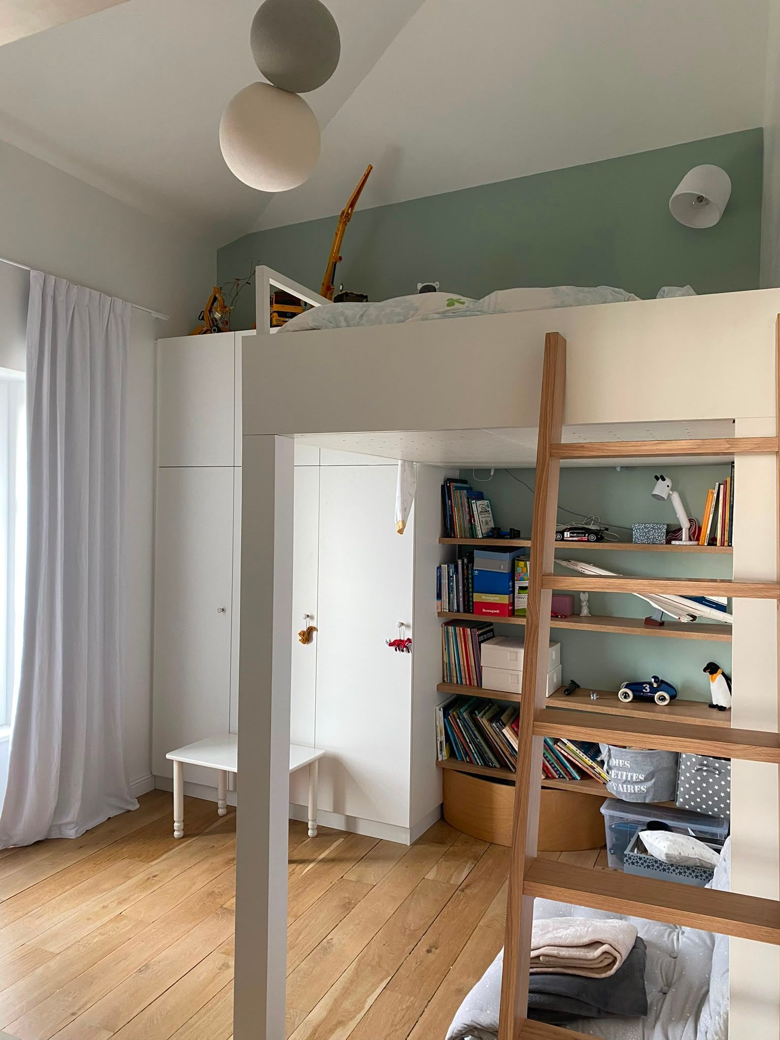 Chambre lumineuse avec lit mezzanine, étagères en bois et rideaux transparents près d’une fenêtre