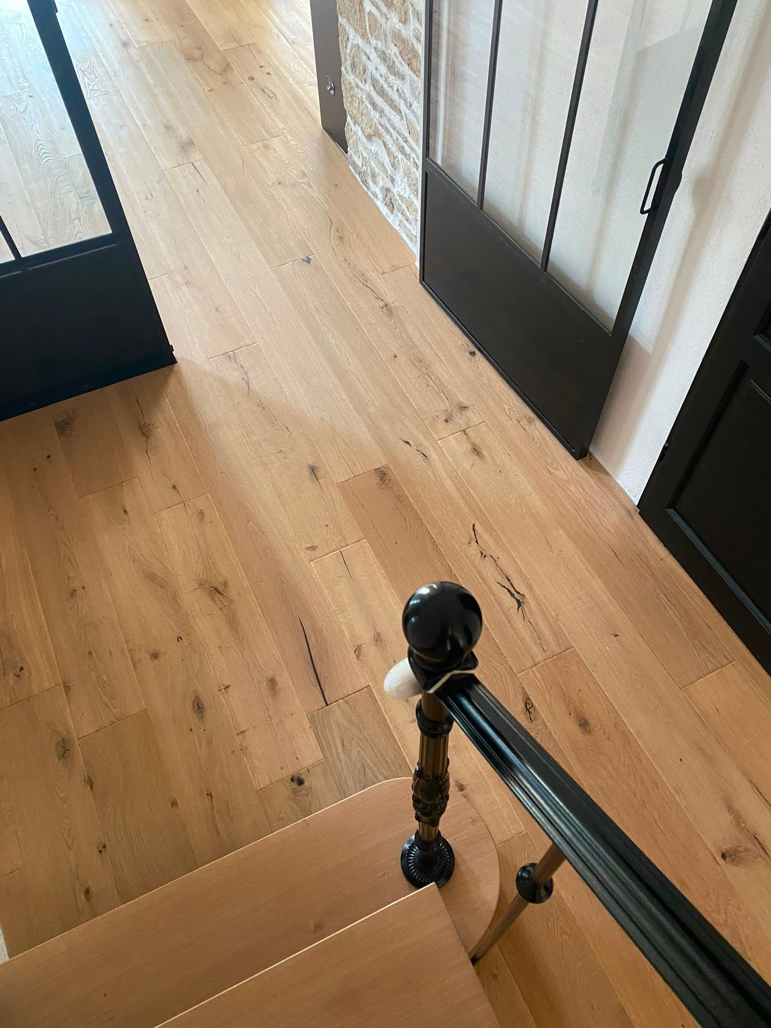 Escalier en bois avec des rampes noires et un palier au sol en bois clair en bas