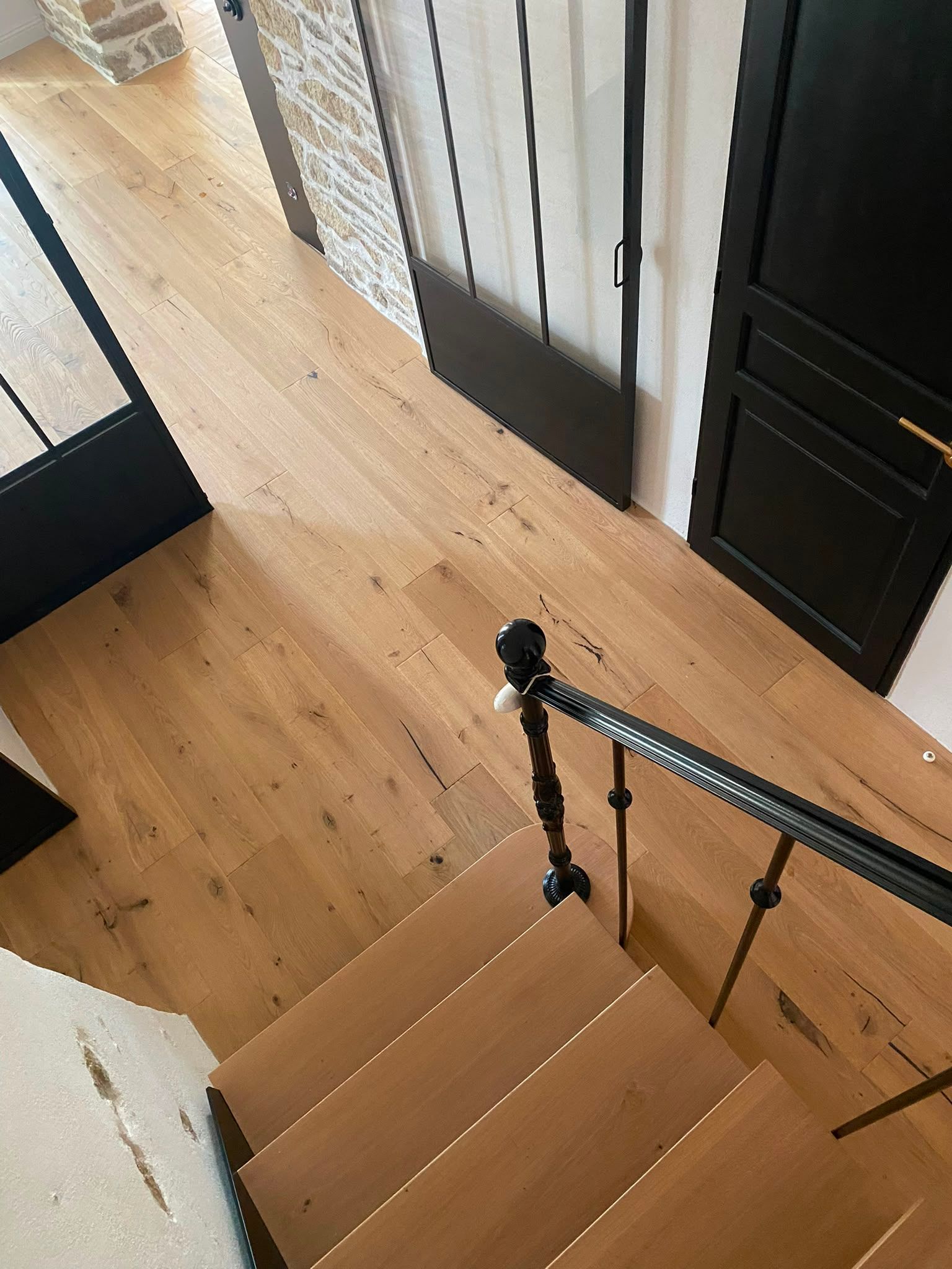 Palier d’escalier en bois avec une rampe noire, à côté de portes blanches et noires, sur un sol en bois clair
