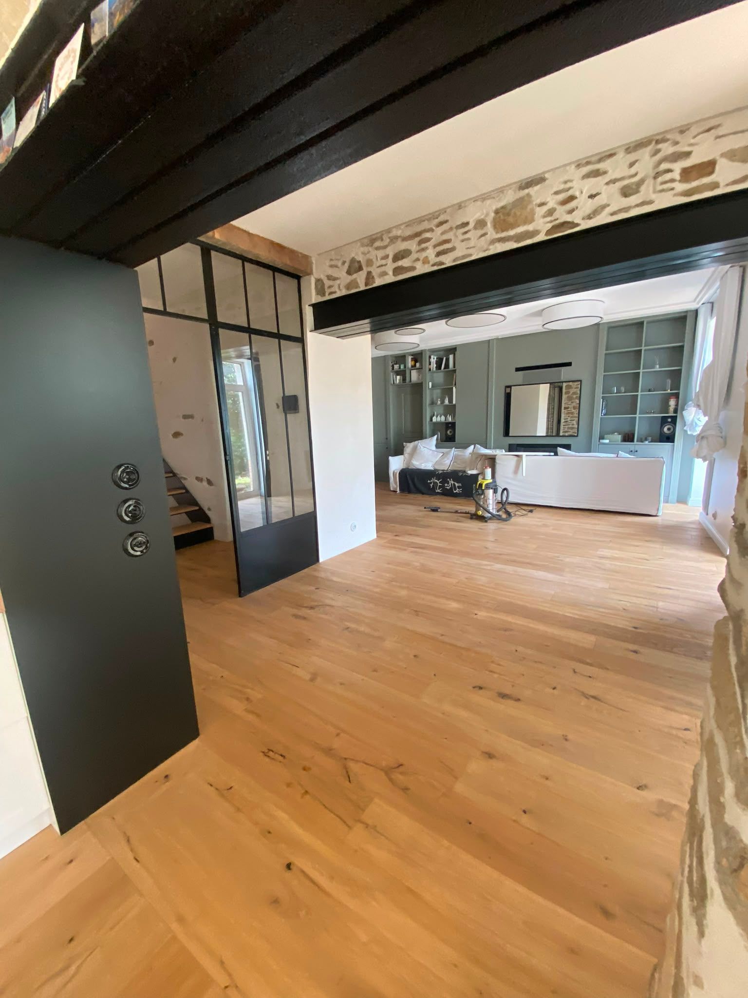 Couloir moderne vide avec un parquet menant à une pièce lumineuse dotée de fenêtres et d’étagères intégrées.