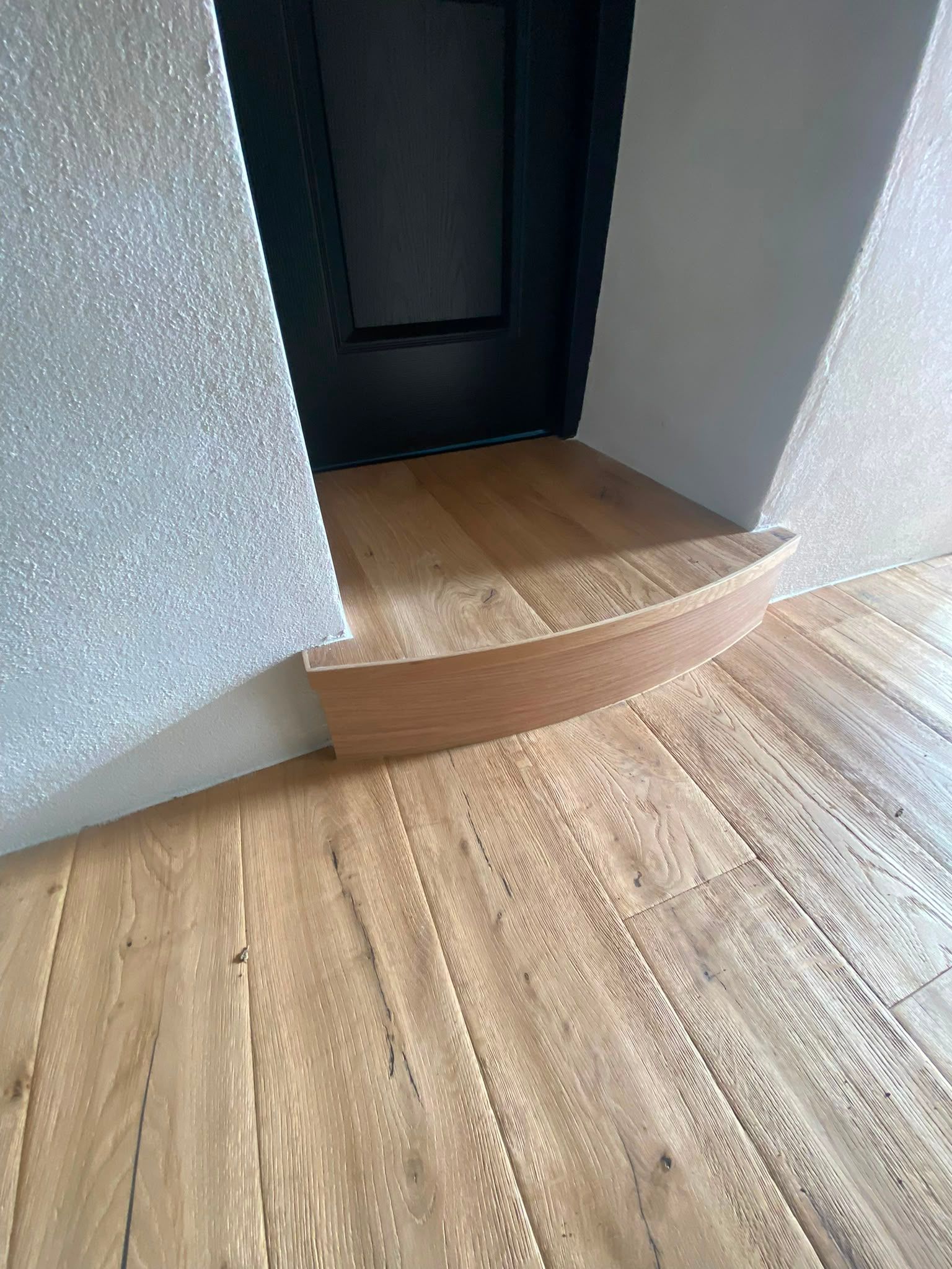 Marche en bois menant à une porte sombre dans un intérieur aux murs clairs