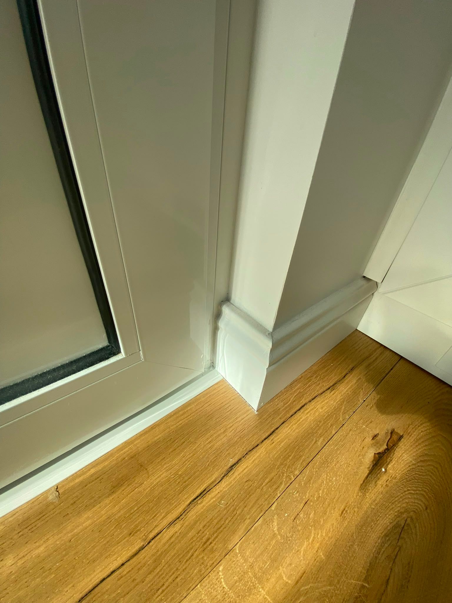 Cadre de porte blanc à côté d’une porte vitrée et d’un angle de parquet