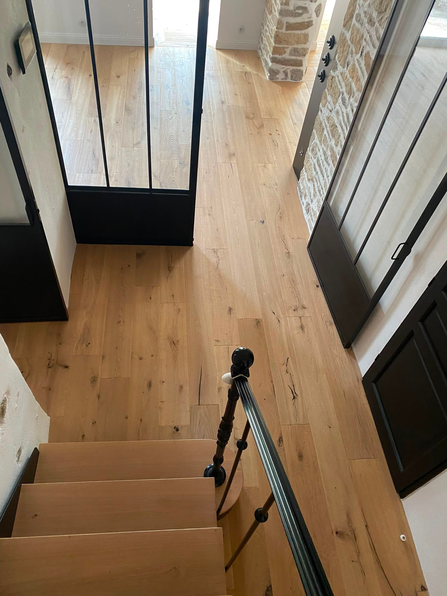 Escalier en bois donnant sur un couloir, avec une rampe noire et un sol en bois clair.