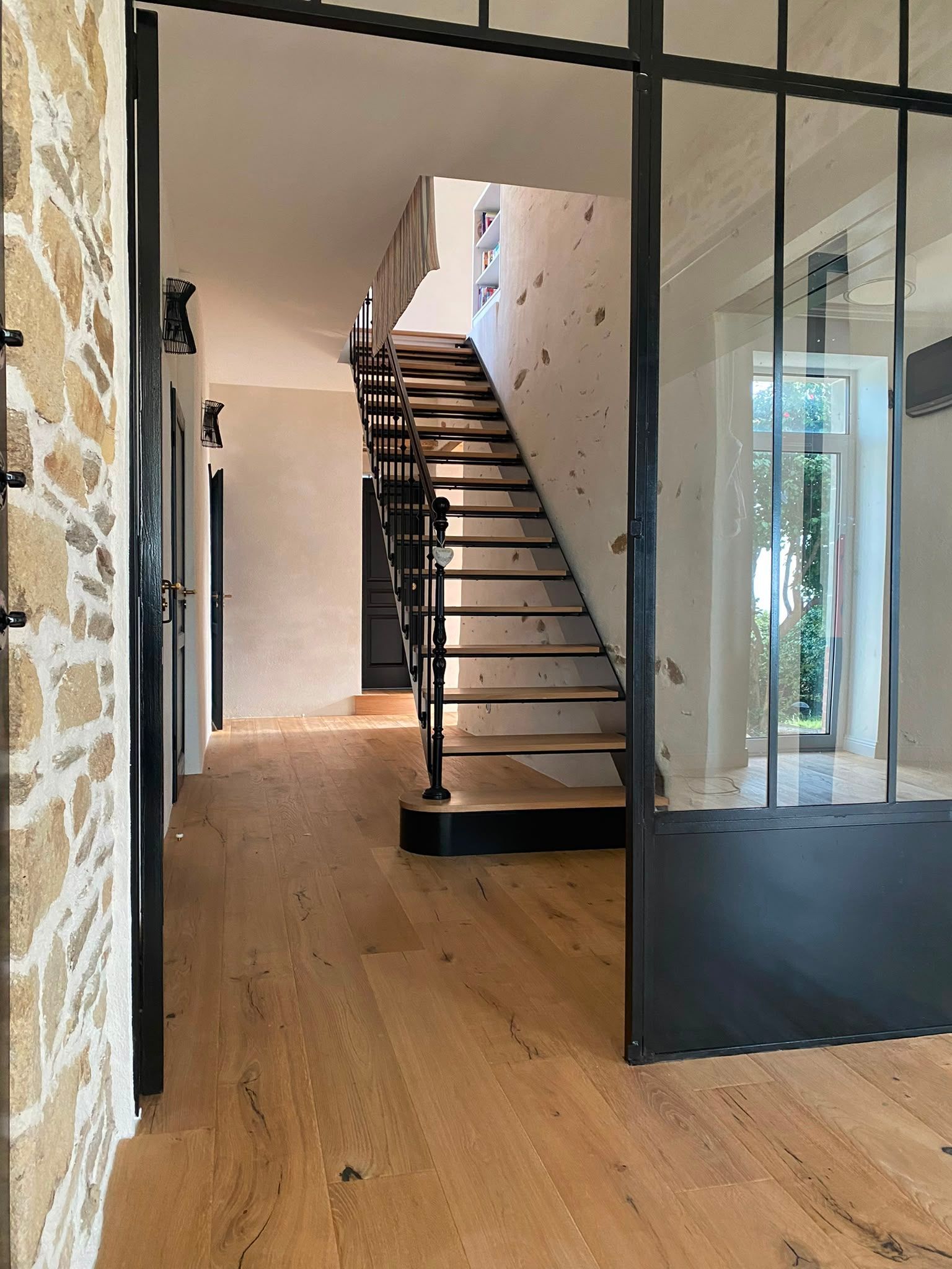 Couloir moderne avec parquet, murs en verre et escalier noir menant à l’étage supérieur