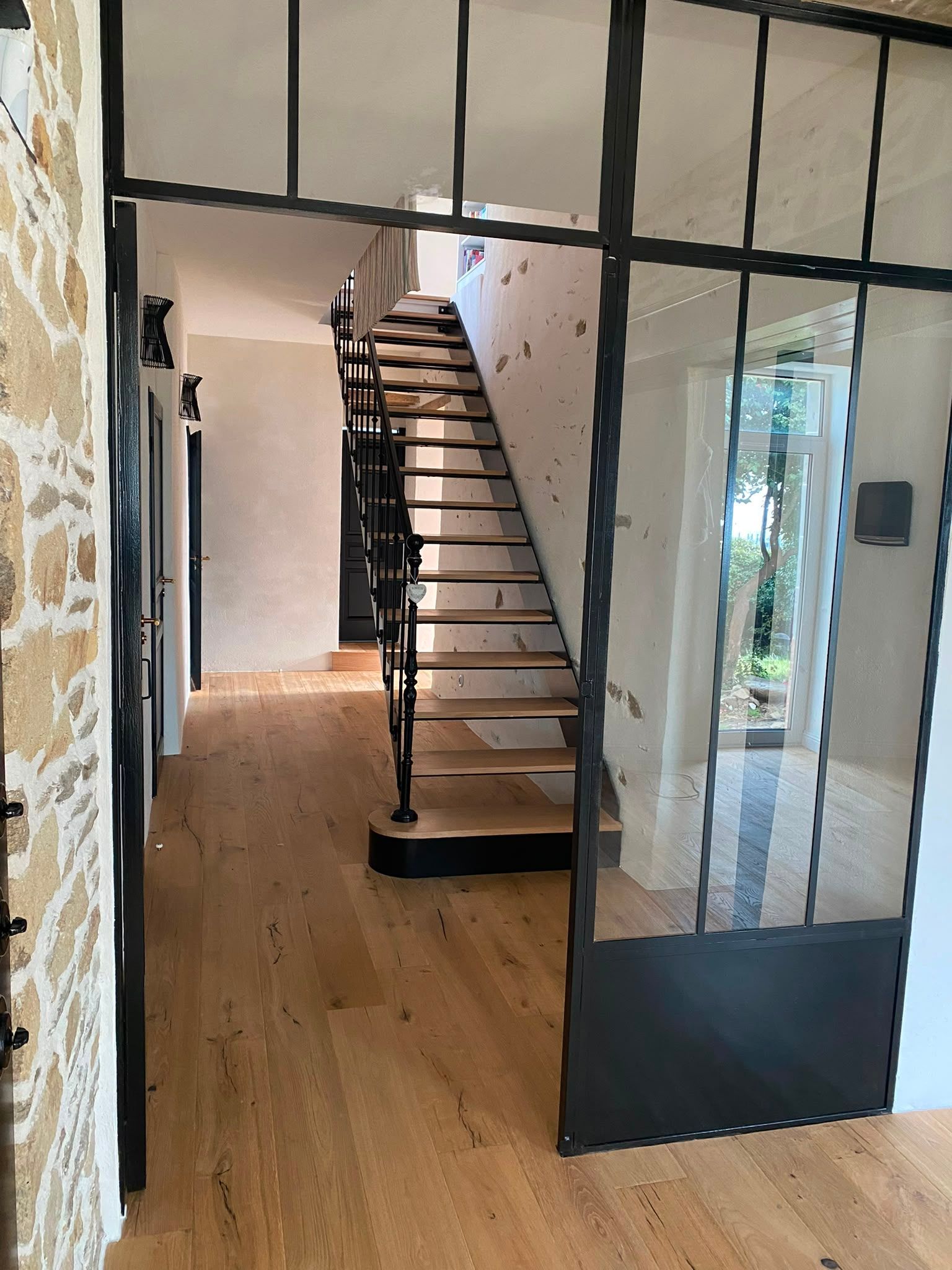 Intérieur moderne avec une cloison vitrée à cadre noir et un escalier en bois dans un couloir
