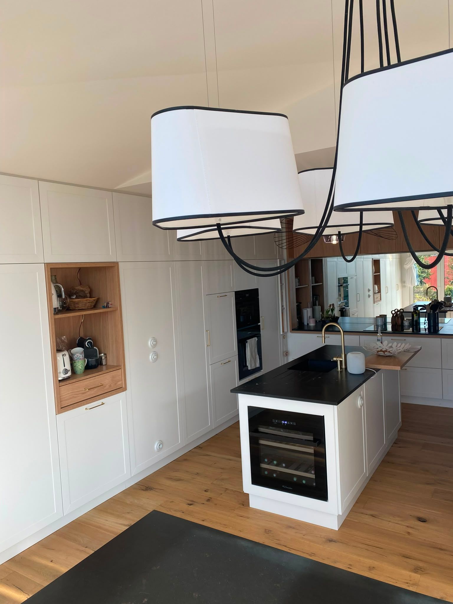 Cuisine moderne avec des placards blancs, un îlot noir, un sol en bois et des suspensions lumineuses