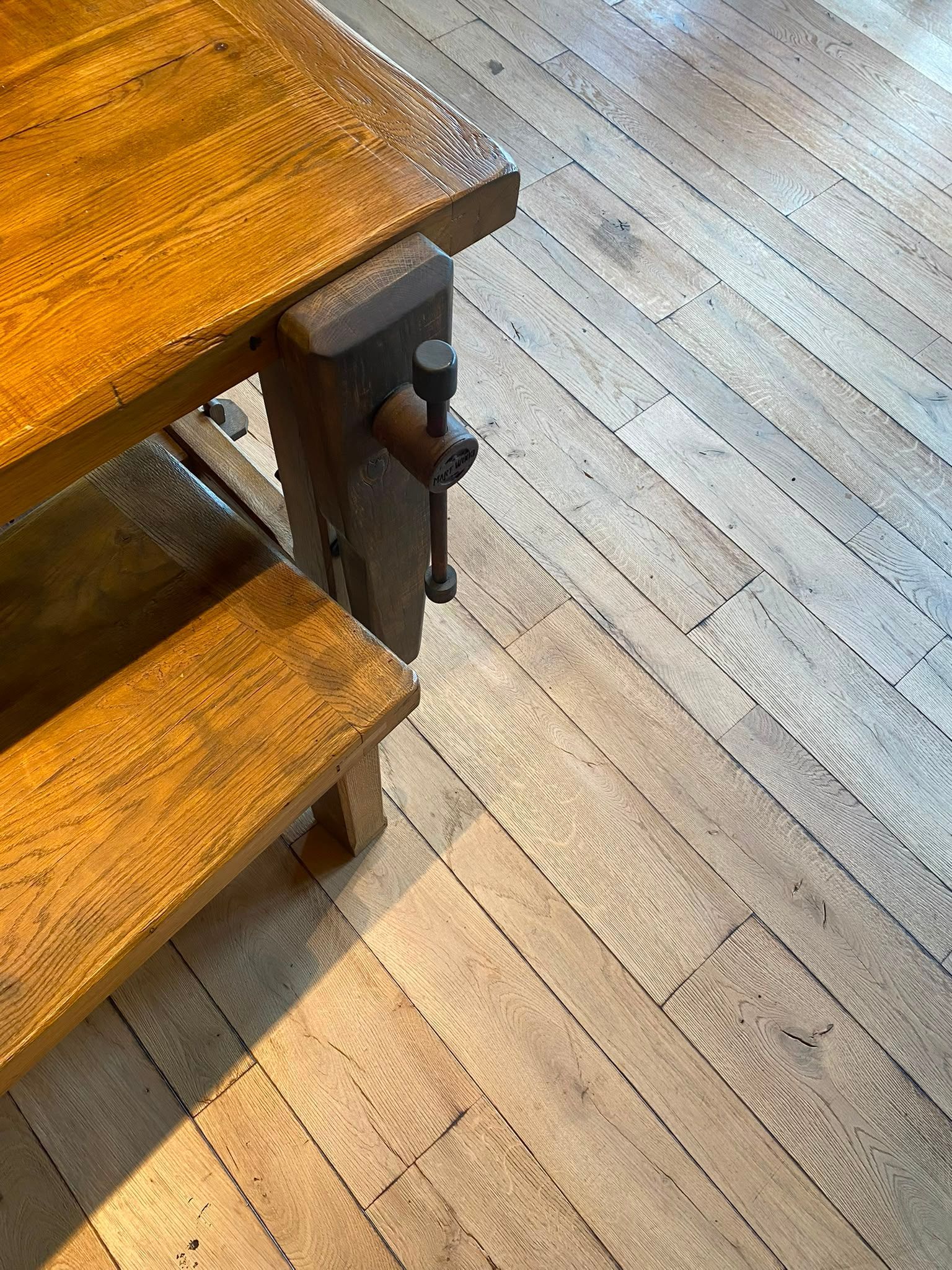 Table et banc en bois à côté d’un sol en lames de bois clair, avec un tabouret en métal foncé sous le bord de la table