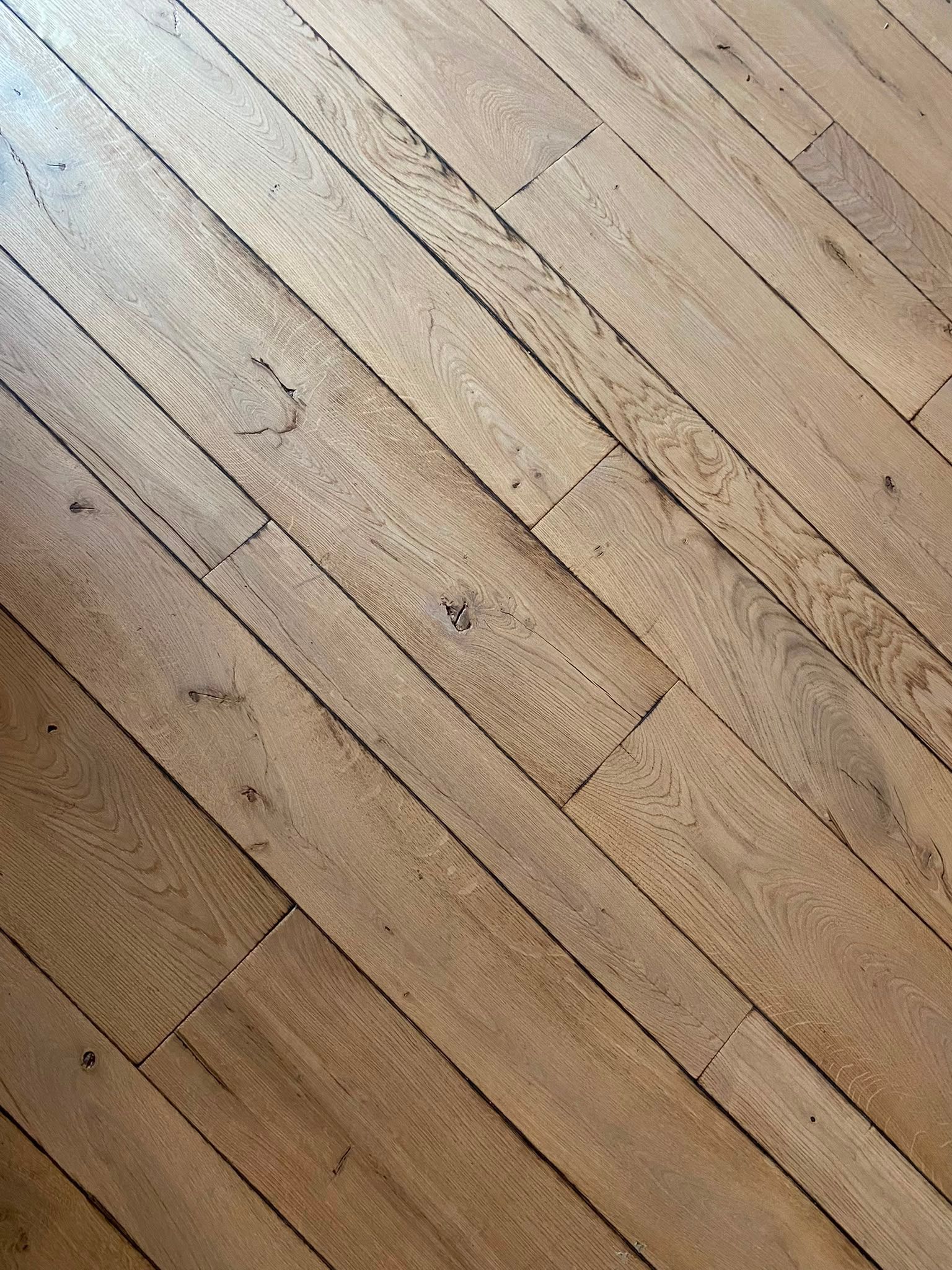 Planches de parquet posées en diagonale, avec des lames usées brun clair et des veines apparentes