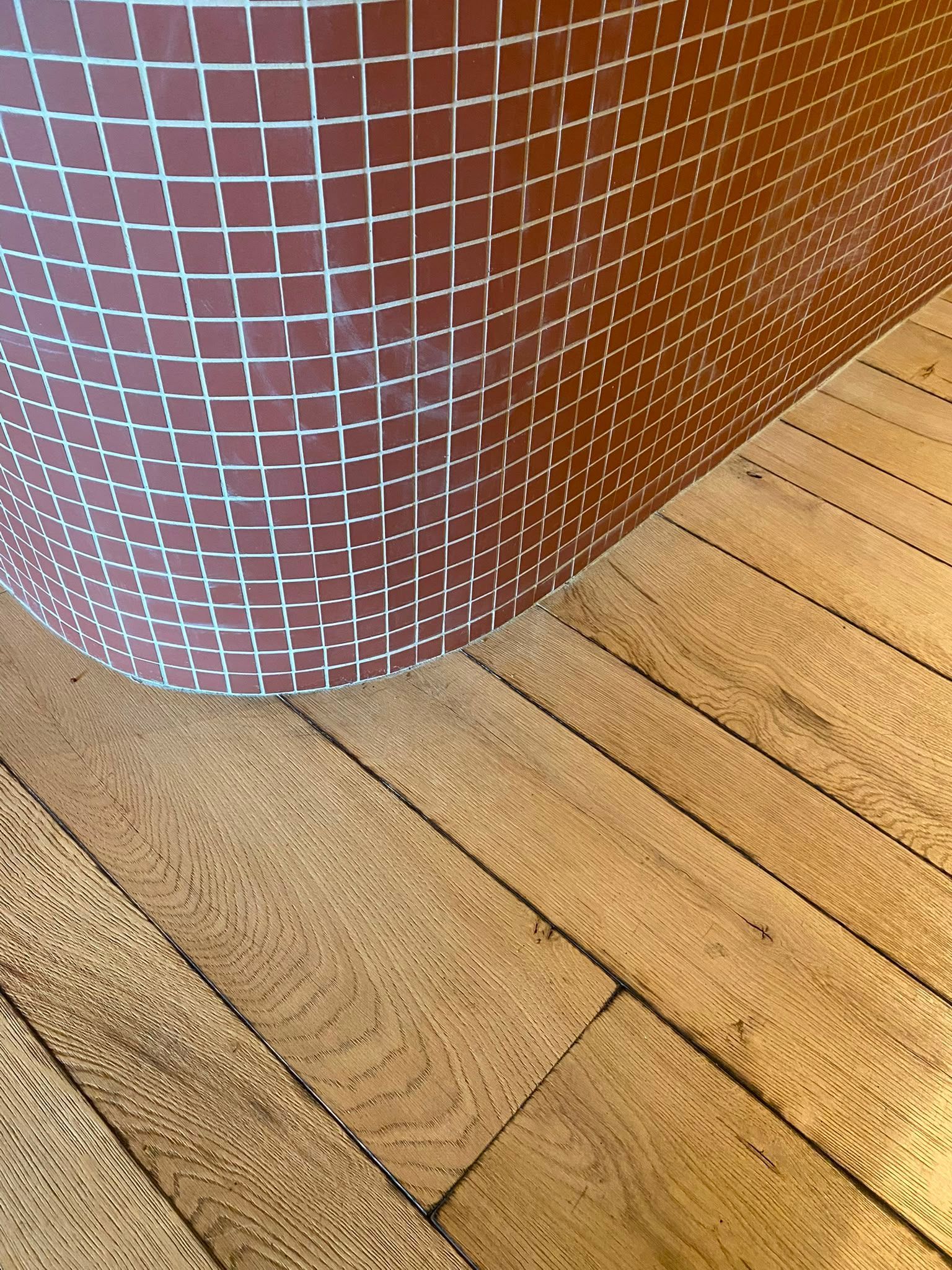 Colonne incurvée recouverte de mosaïque rouge, à côté d’un parquet clair