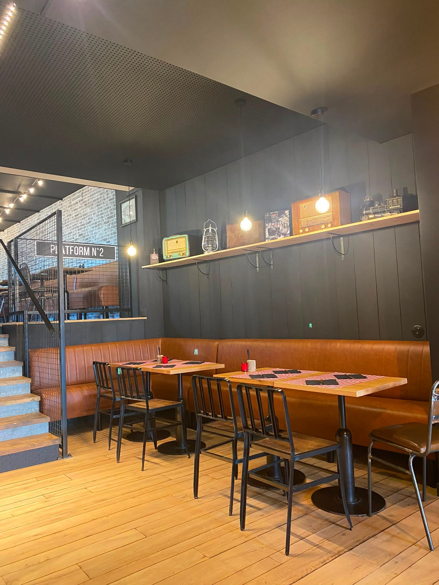 Intérieur moderne de restaurant avec des tables en bois, des chaises noires, un escalier et un éclairage mural chaleureux