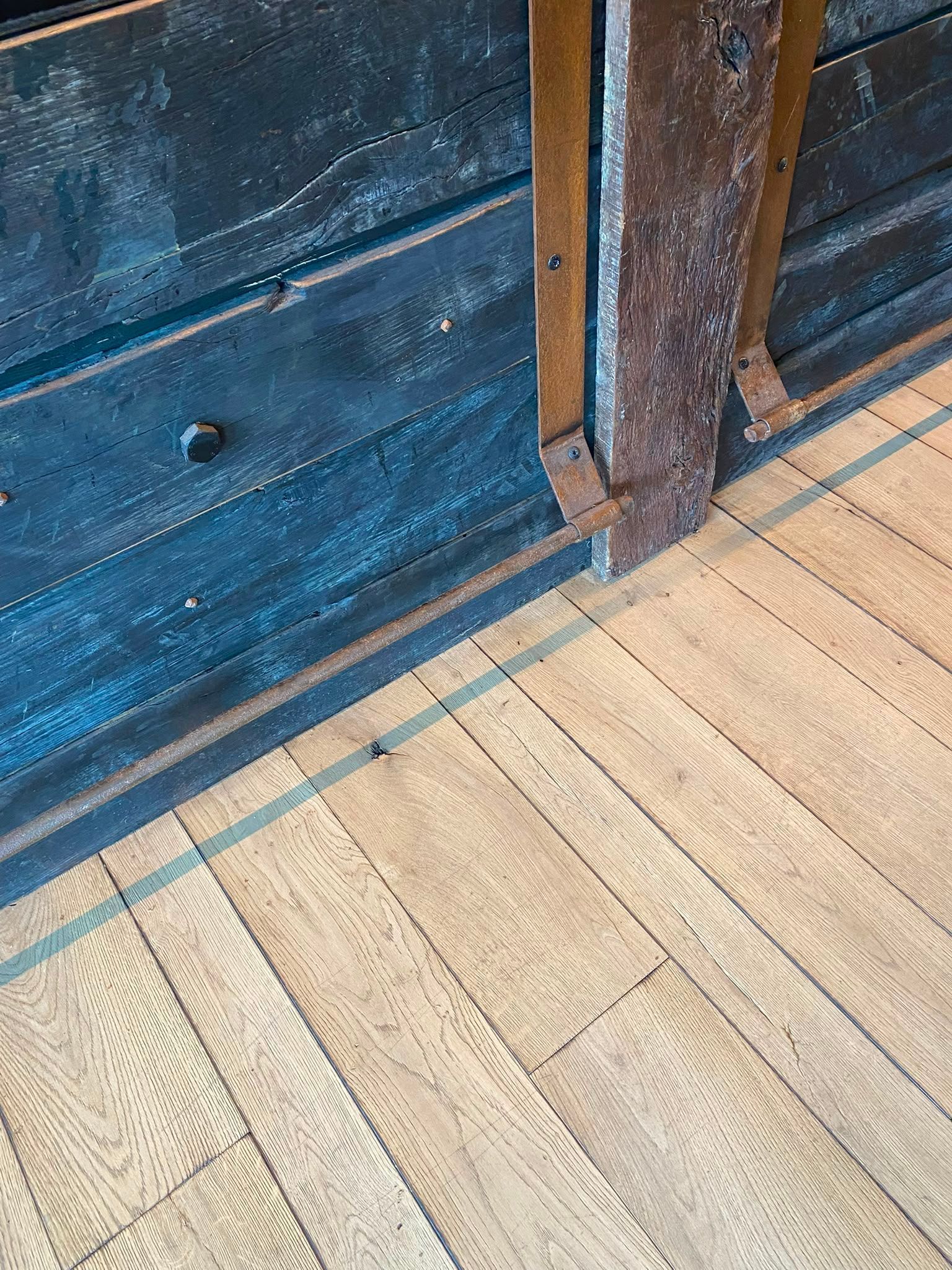 Parquet rejoignant un mur bleu foncé et un poteau en bois brun dans un angle.
