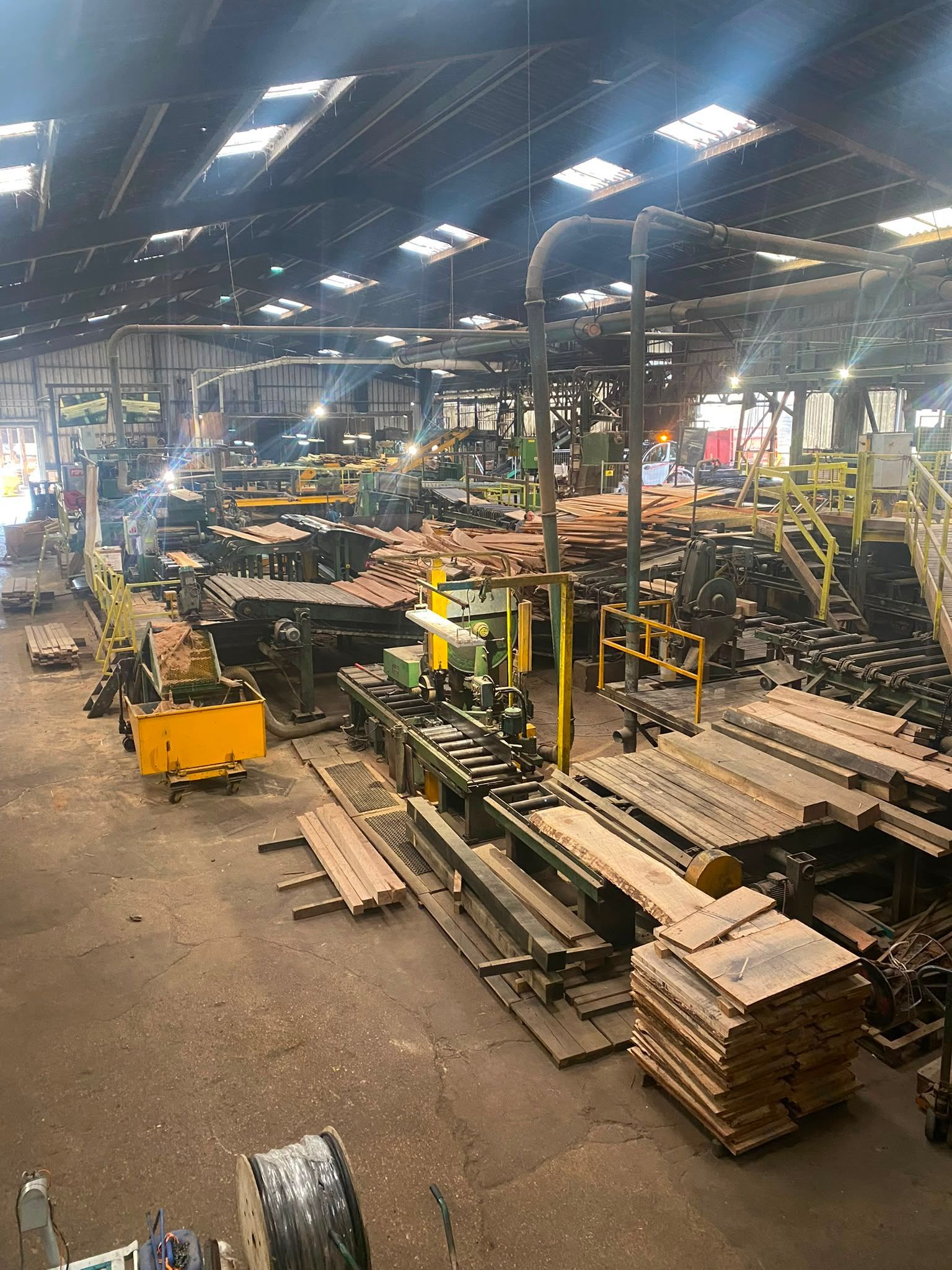 Grand entrepôt industriel avec des rangées de palettes, des machines et un éclairage suspendu