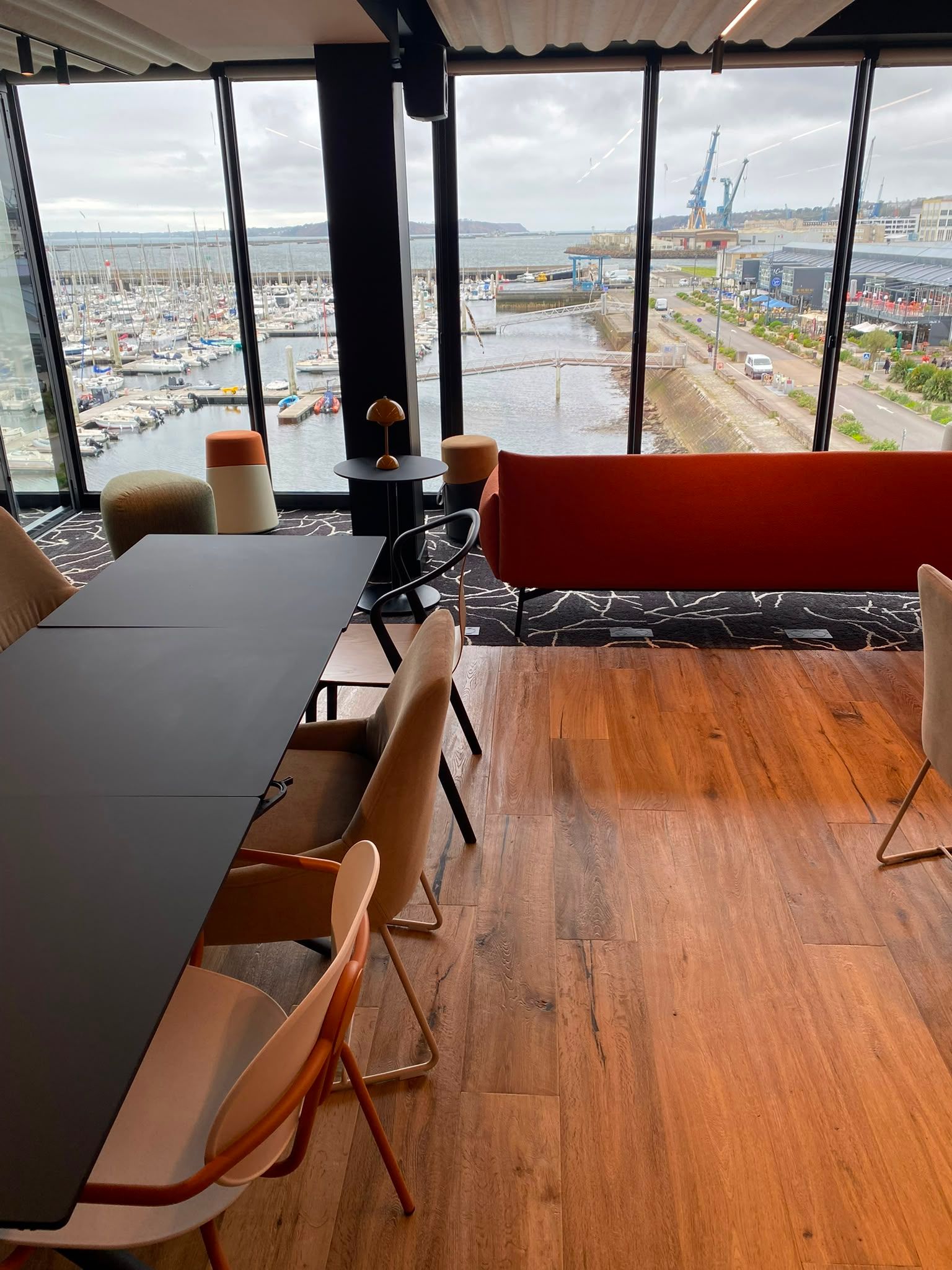 Restaurant sur le toit avec des tables et des chaises donnant sur une ville portuaire et son port.