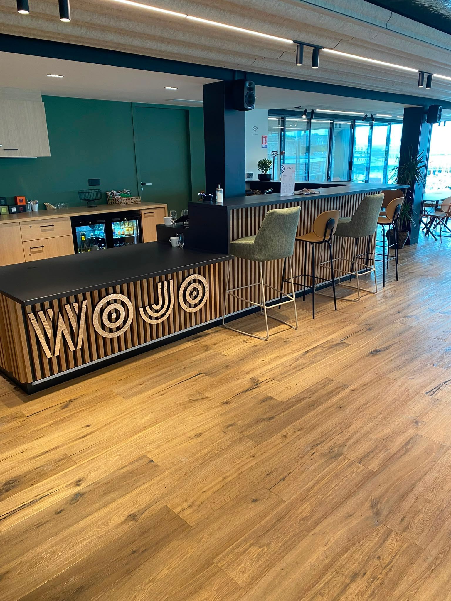 Comptoir de café moderne avec des tabourets, un parquet, des murs bleu sarcelle et de grandes fenêtres donnant sur la rue