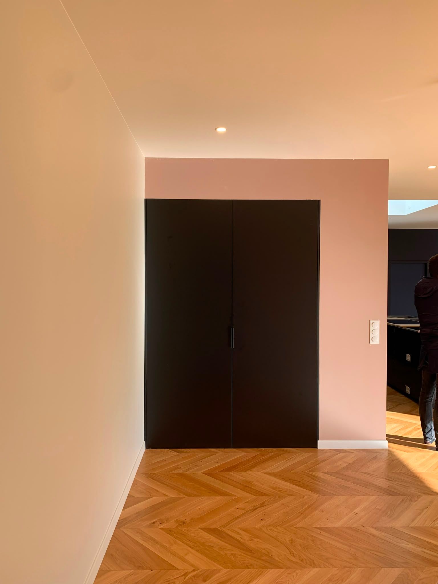 Couloir avec parquet en chevrons et grandes portes doubles foncées sur des murs clairs