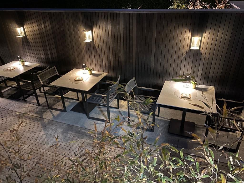 Terrasse extérieure avec des tables et des chaises vides, éclairée chaleureusement par des lanternes murales la nuit