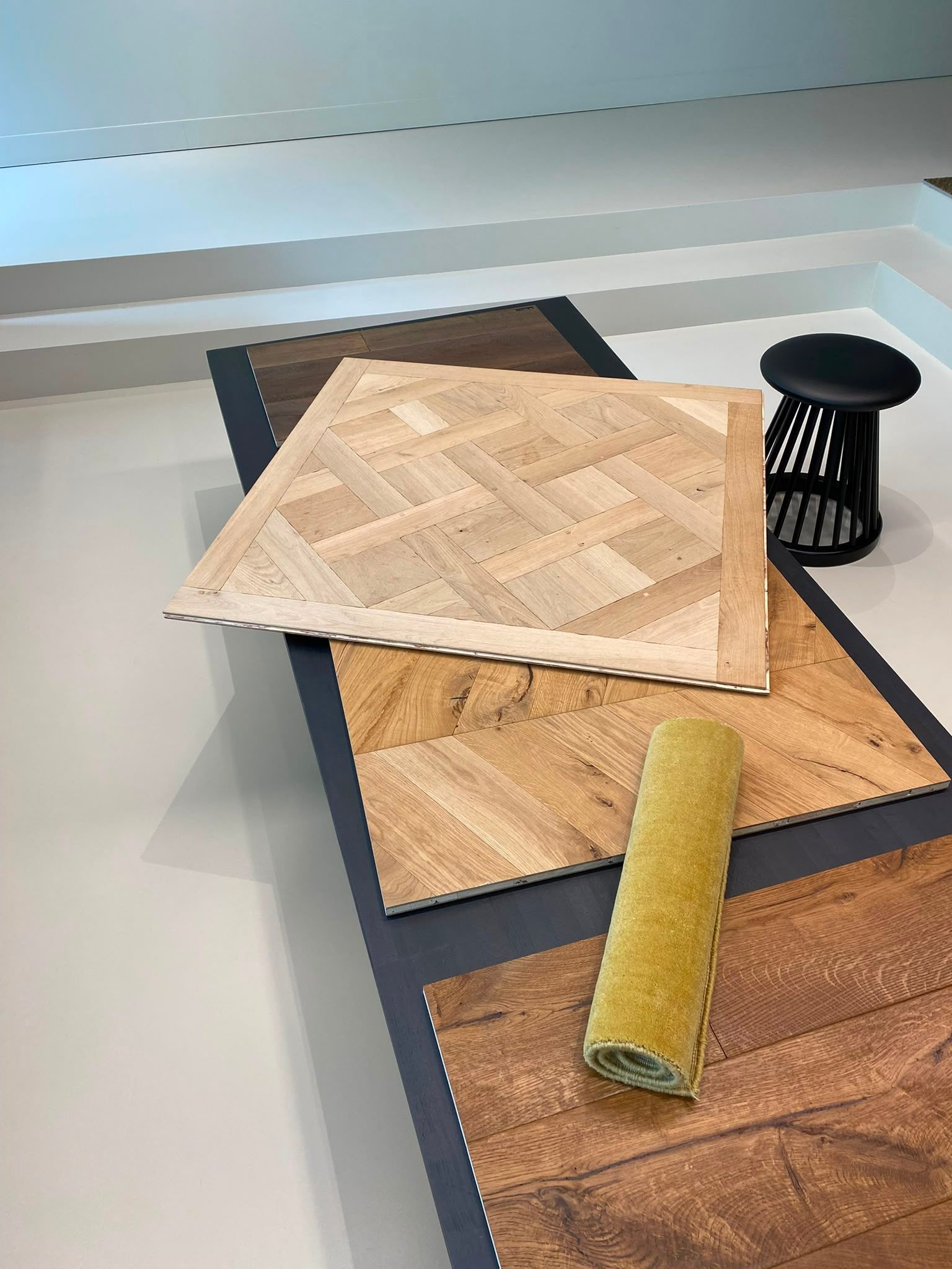 Trois échantillons de parquet sur une table, avec un rouleau cylindrique jaune à côté.