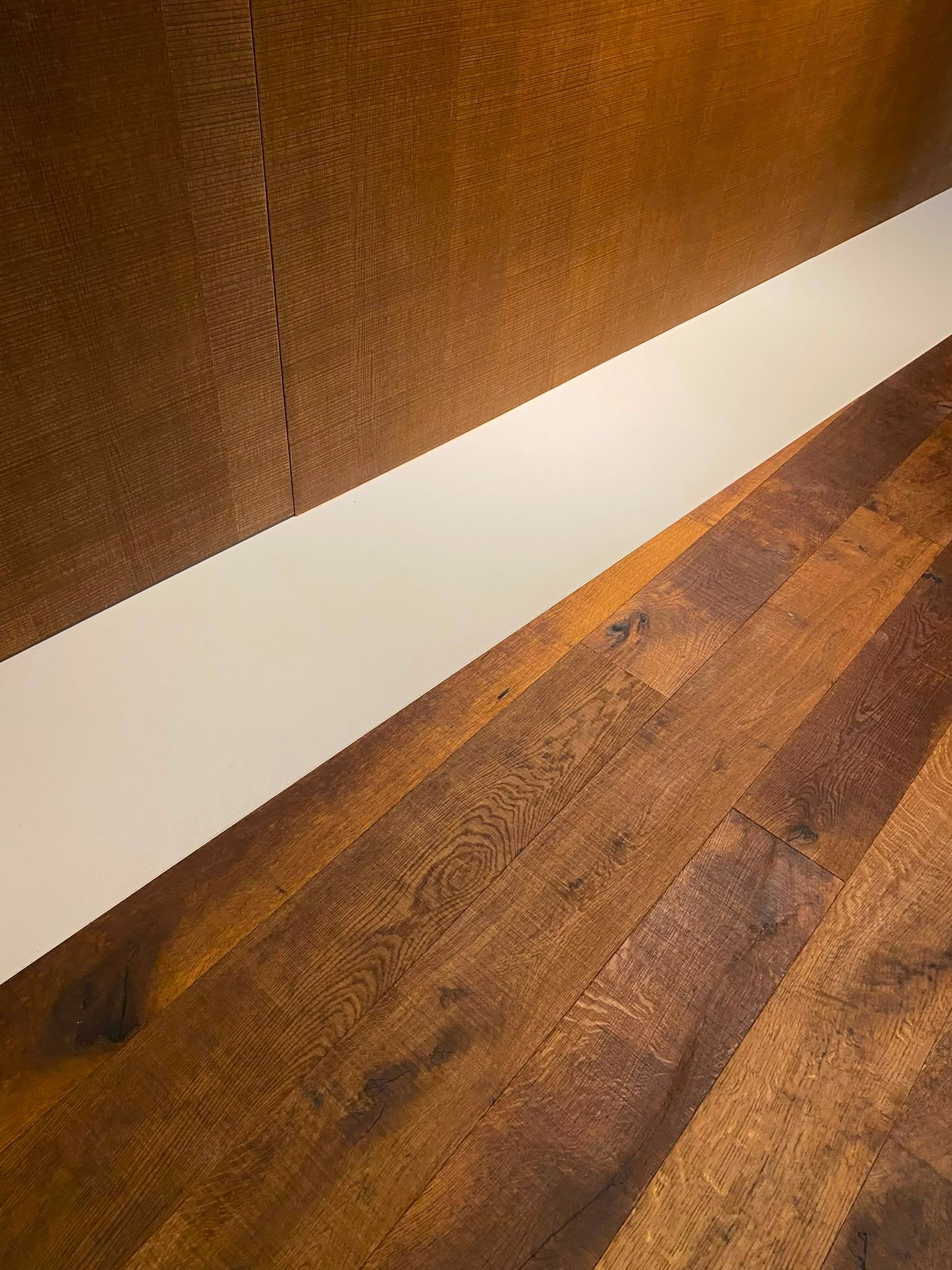 Parquet près d’un mur blanc avec un panneau texturé marron et une lumière vive qui éclaire le couloir