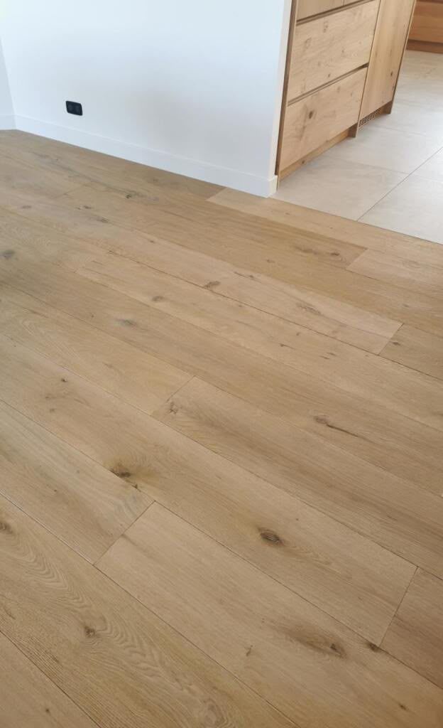 Parquet clair dans une pièce lumineuse aux murs blancs, avec une porte en bois ouverte.