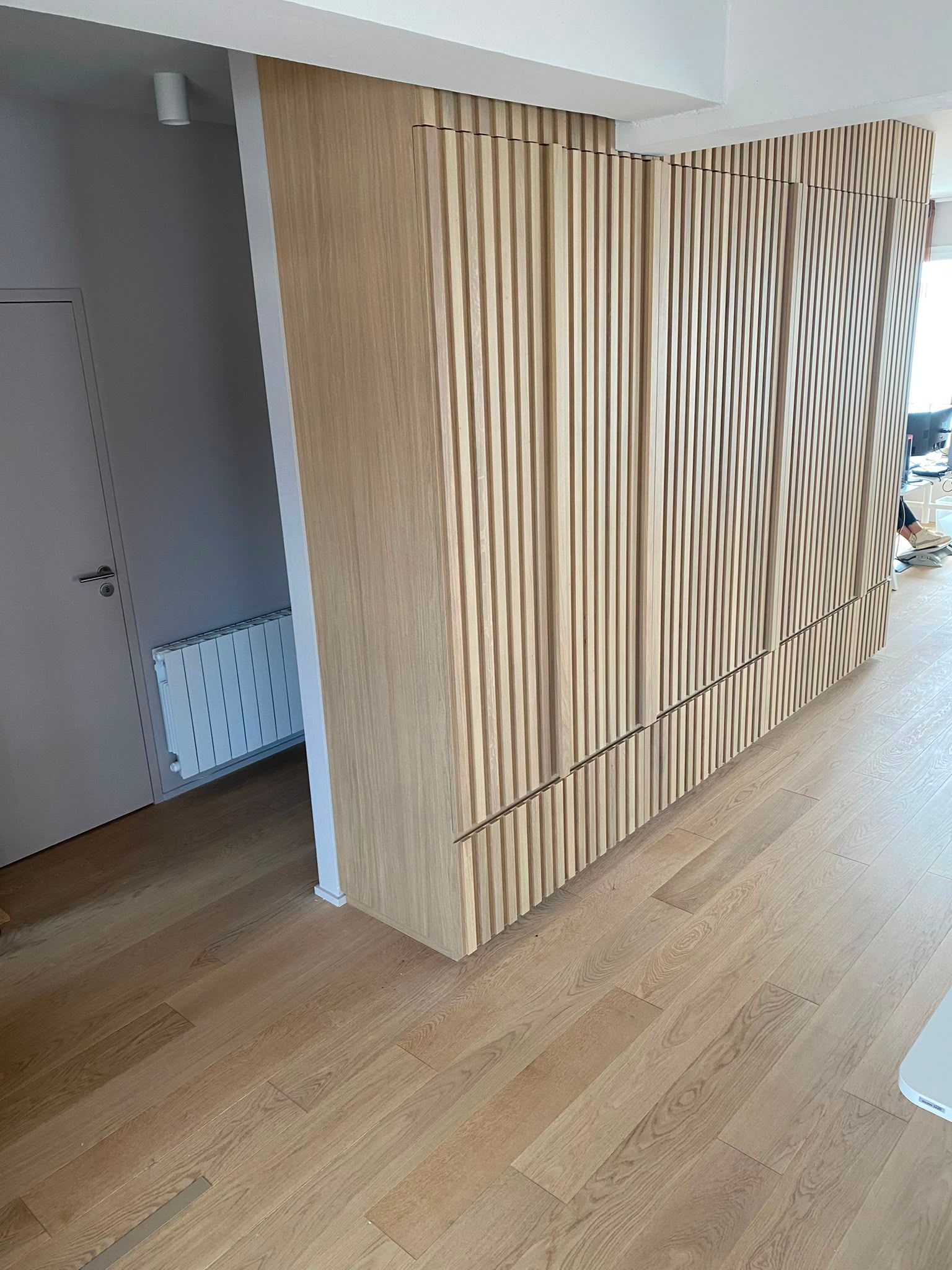 Cloison à lattes de bois dans un couloir lumineux, avec un parquet et une porte ouverte à proximité