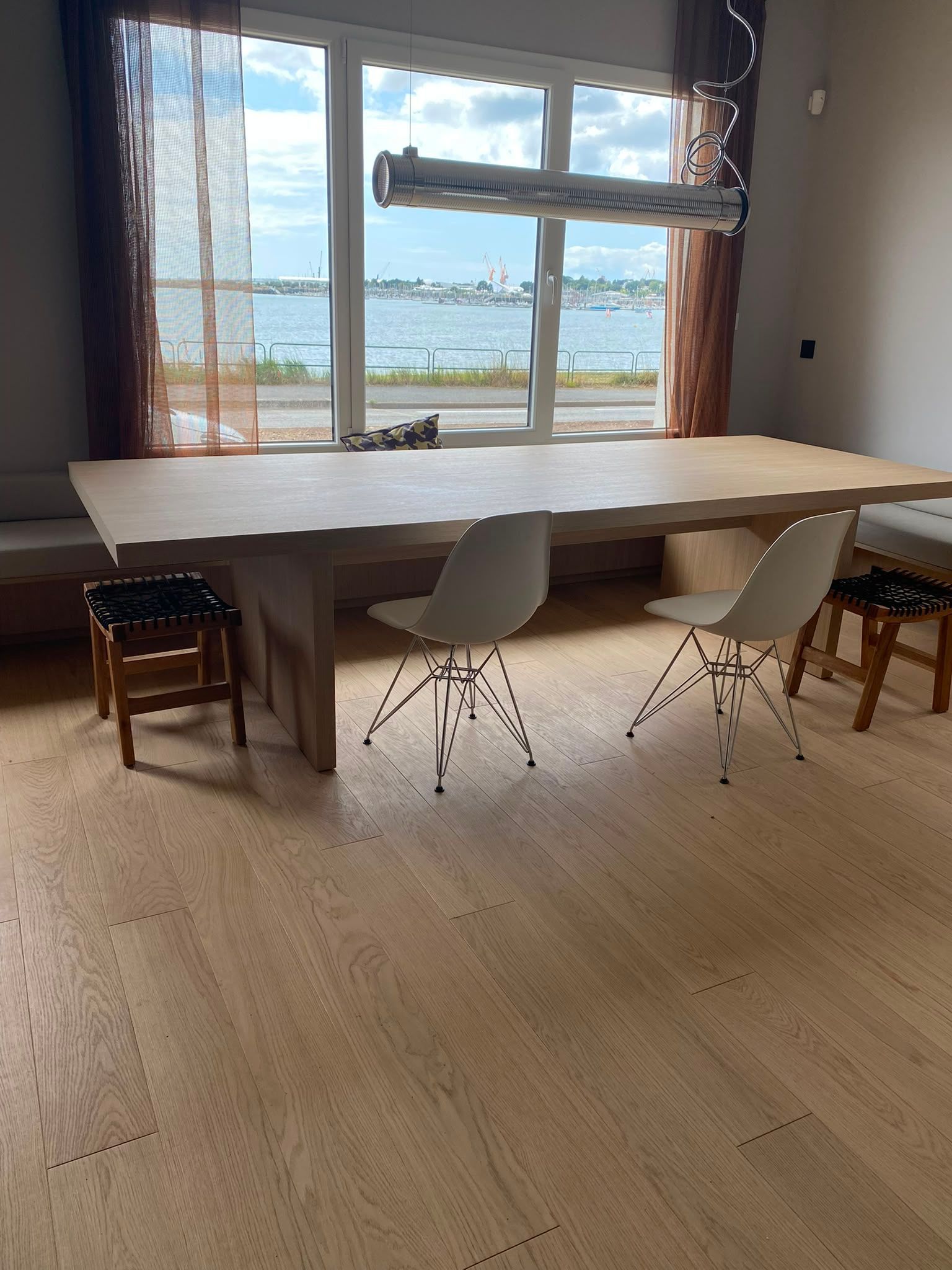 Pièce lumineuse avec une longue table, trois chaises et de grandes fenêtres donnant sur le front de mer.