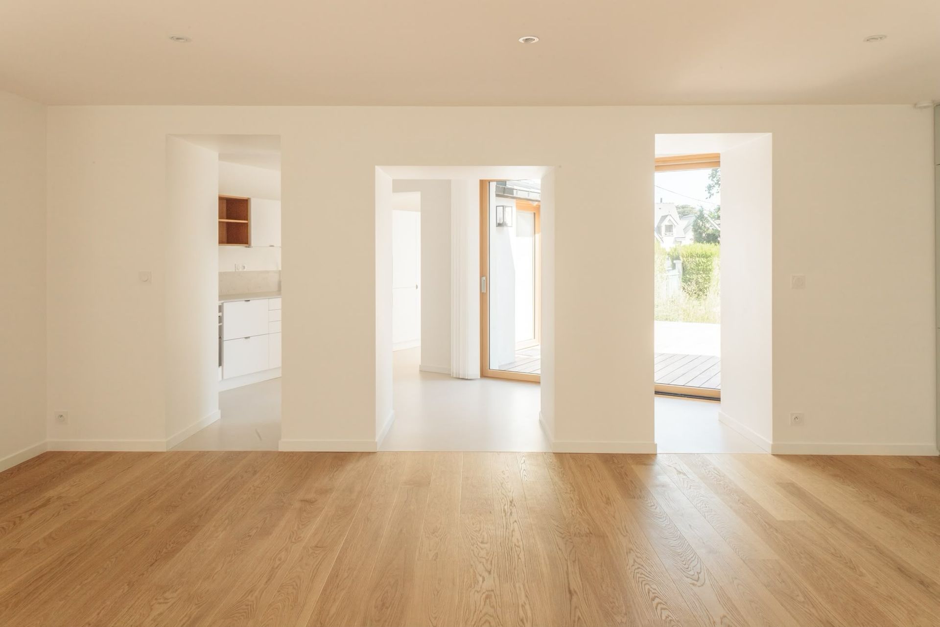 Pièce lumineuse et vide, avec un parquet clair et des murs blancs