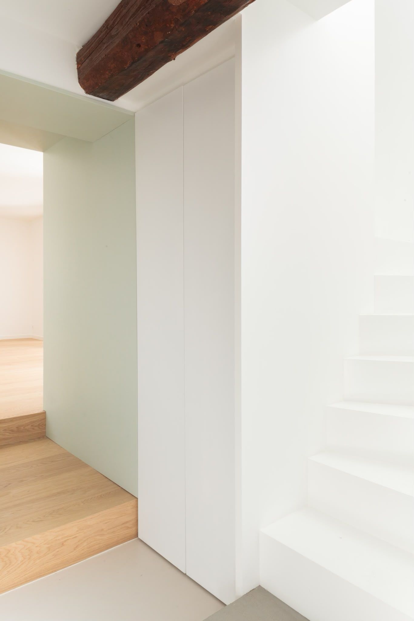 Couloir minimaliste blanc avec parquet, poutre apparente et petit escalier à droite