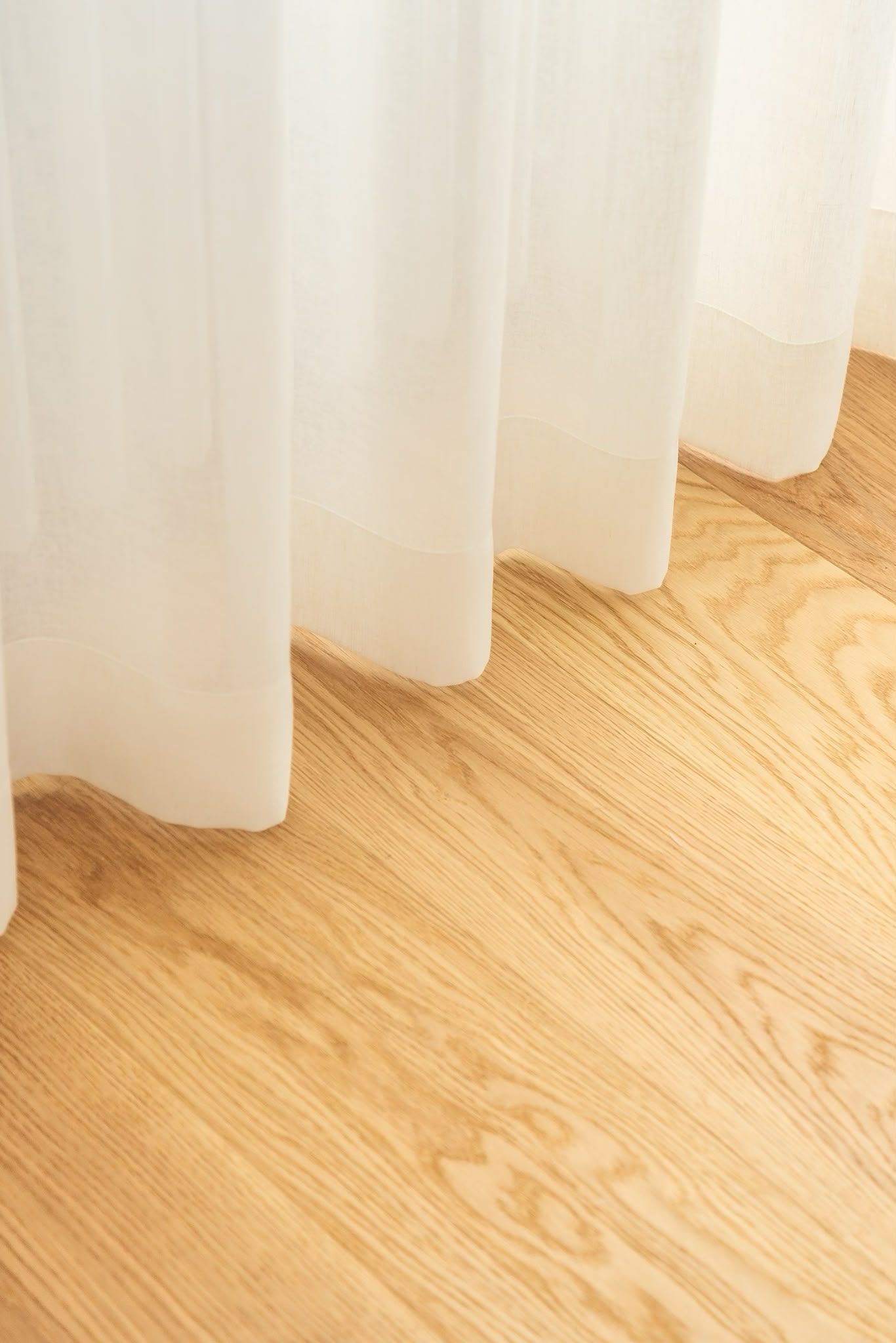 Des voilages blancs au-dessus d’un parquet clair, baignés d’une douce lumière naturelle