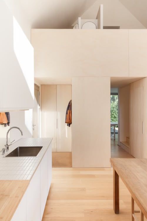 Cuisine lumineuse et minimaliste, avec parquet, meubles blancs, table en bois et mezzanine
