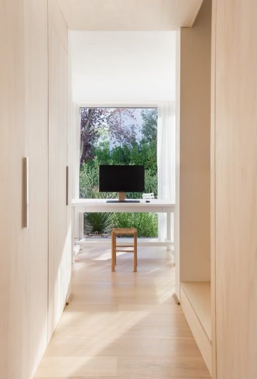 Couloir minimaliste avec un bureau blanc, un tabouret et une vue sur la verdure depuis la fenêtre