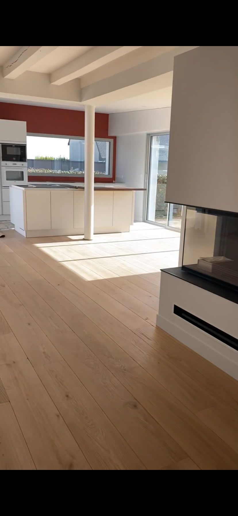 Cuisine et séjour modernes et lumineux, avec parquet, meubles blancs et soleil qui inonde la pièce.