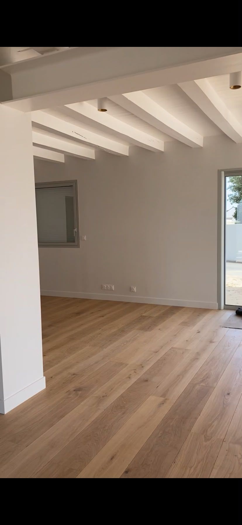 Pièce moderne vide avec parquet, poutres apparentes au plafond et porte donnant sur l’extérieur.