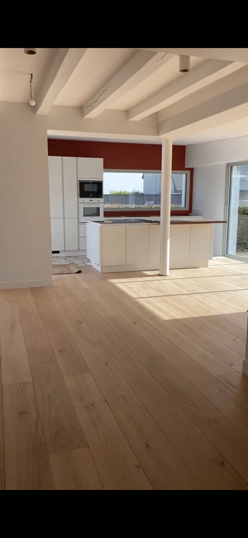 Pièce lumineuse et vide avec un parquet, des poutres apparentes et un petit coin cuisine au fond