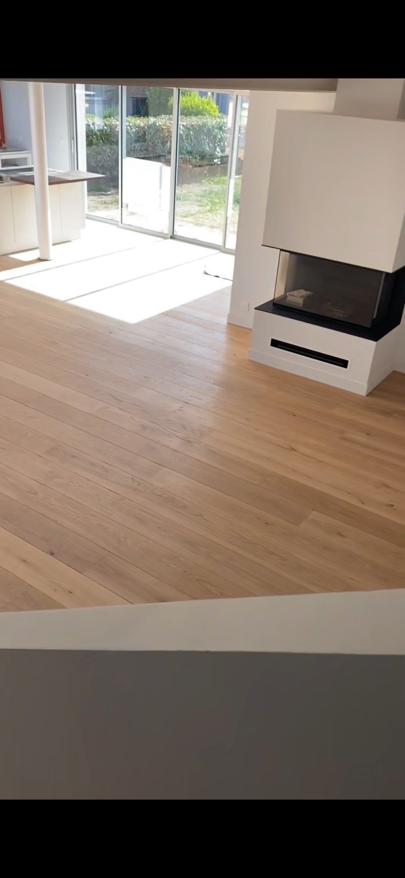Salon moderne vide avec parquet, cheminée blanche et baies vitrées coulissantes donnant sur une terrasse.