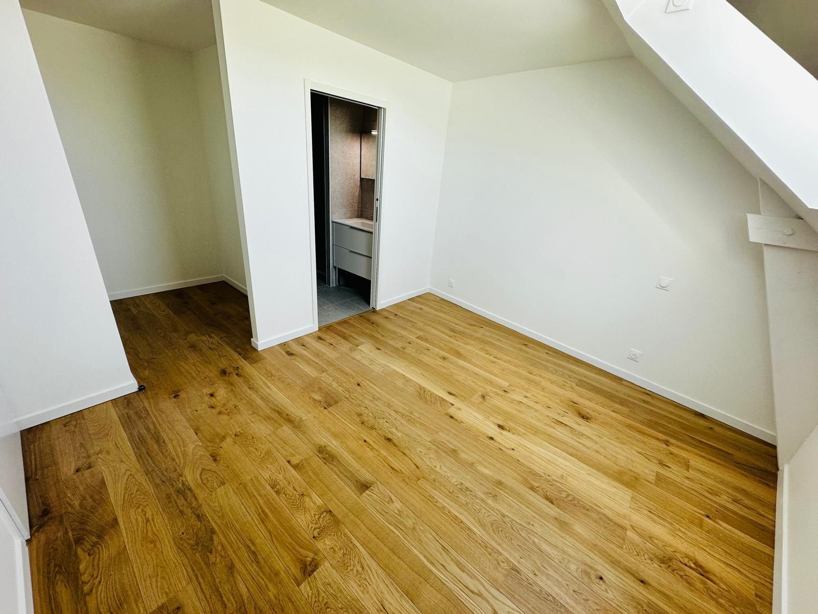Pièce mansardée vide avec un parquet clair, des murs blancs et une porte donnant sur un petit placard.
