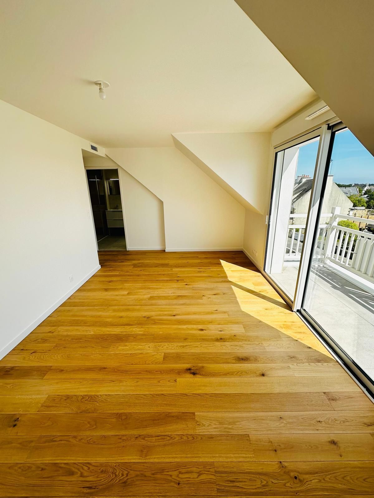 Pièce lumineuse et vide, avec un parquet et un plafond en pente