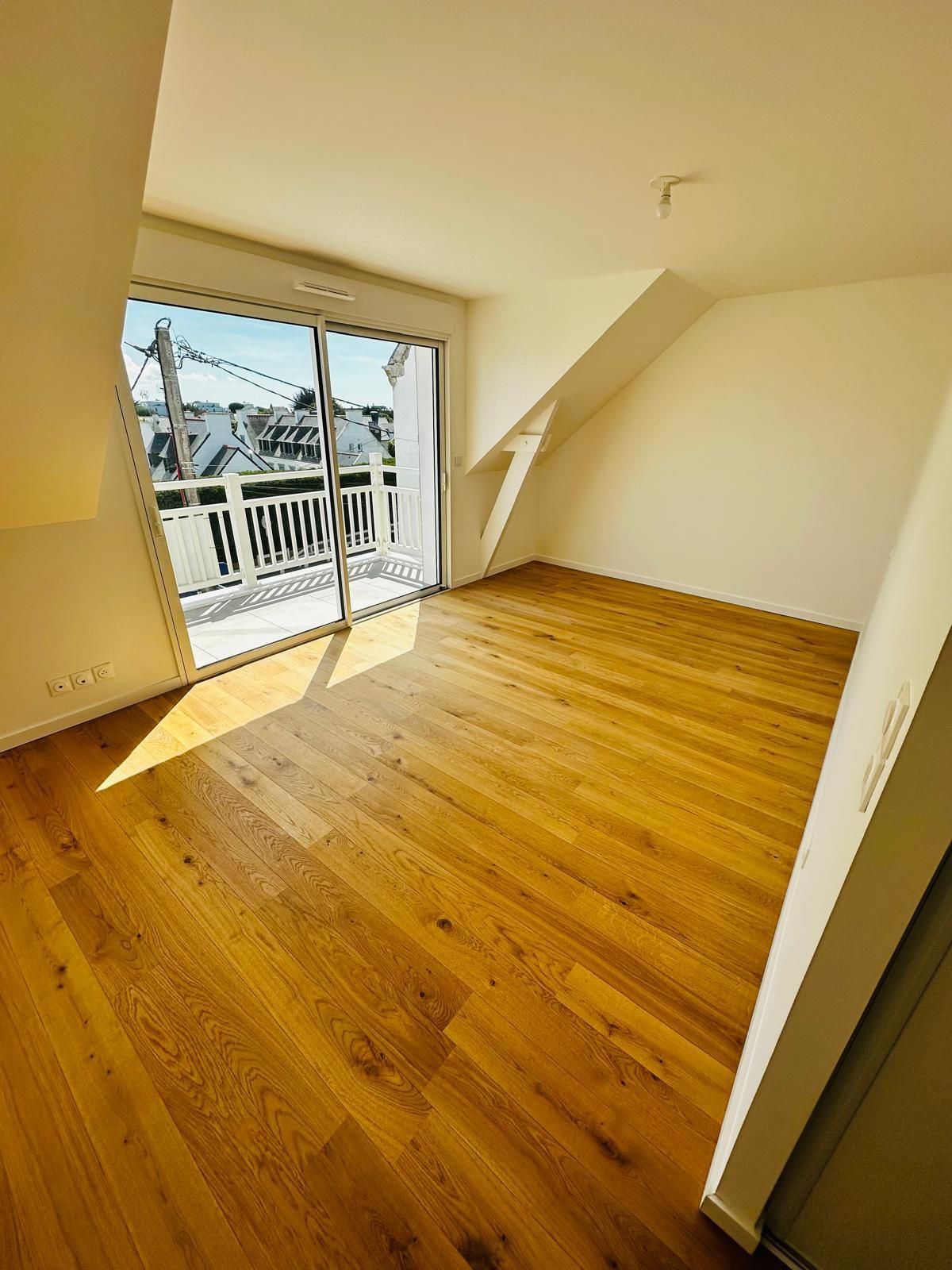 Pièce vide baignée de soleil, avec un parquet et une porte de balcon ouverte donnant sur des toits enneigés