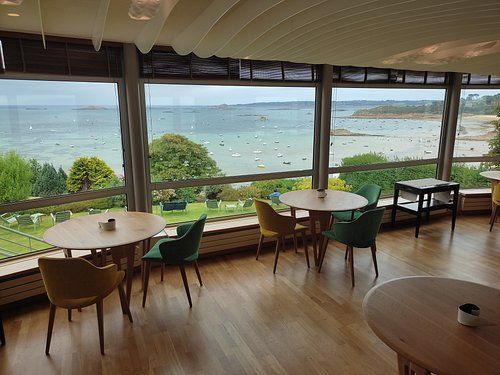Café en bord de mer avec des tables rondes, des chaises en bois et de grandes fenêtres donnant sur l’océan